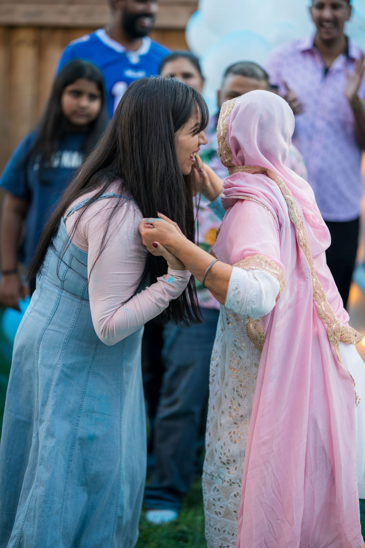 Two women in traditional South Asian attire share an intimate forehead-to-forehead moment at an outdoor event.