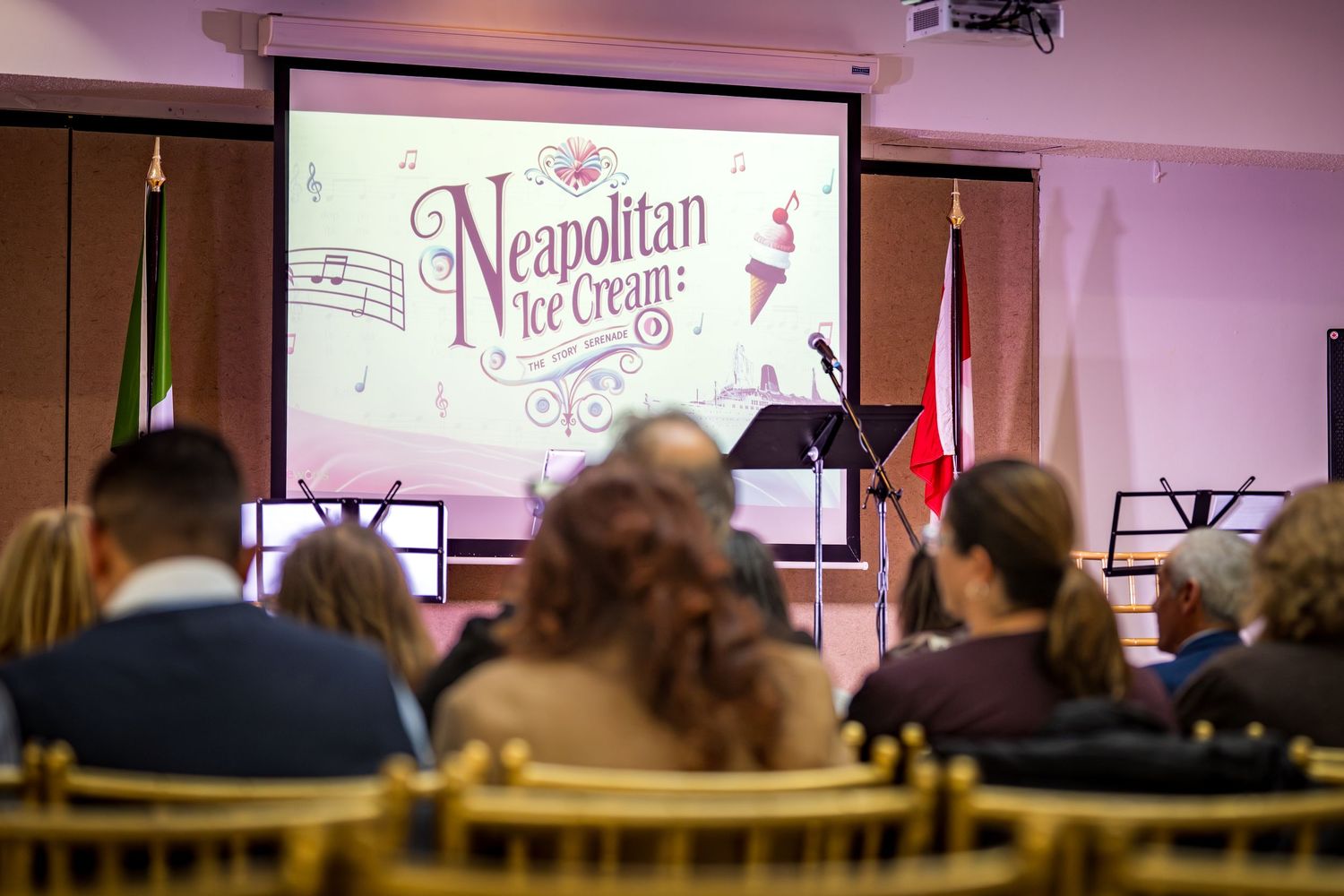 Audience seated at a Neapolitan Ice Cream themed event with a decorative presentation screen displayed at the front.