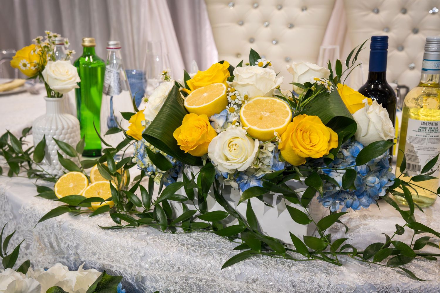 Wedding sweetheart table centerpiece with yellow roses, white flowers, lemons, and lush greenery arrangement.