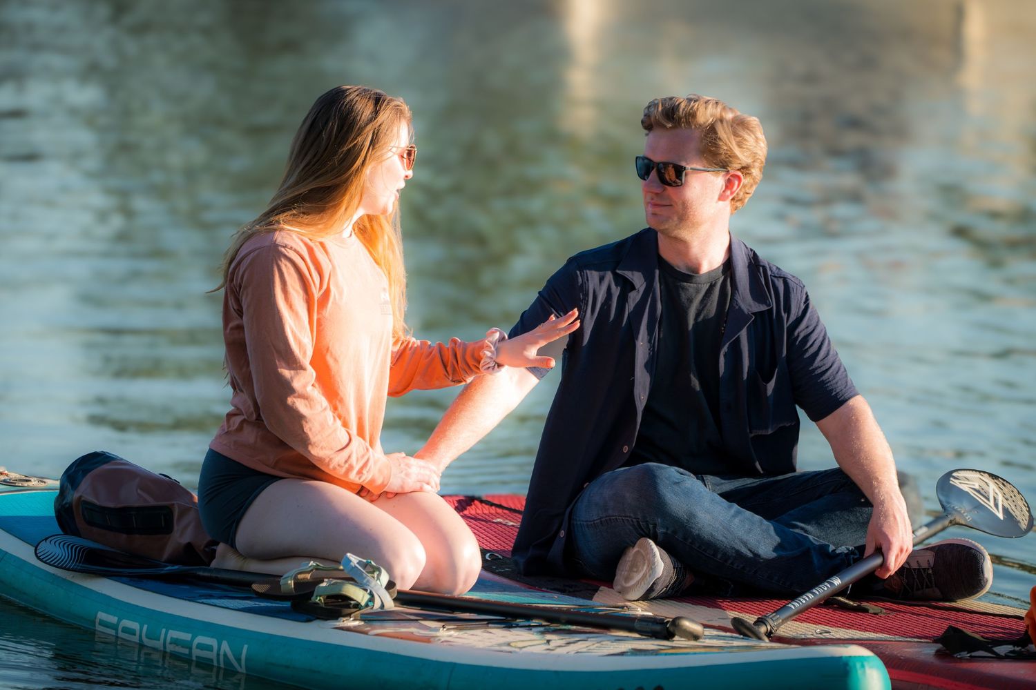 Couple sitting on a paddleboard on a calm lake, sharing a romantic moment together.