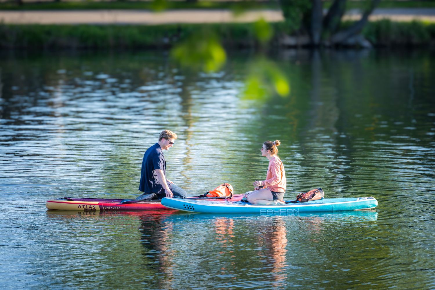 Two people sitting on paddleboards on a calm lake surrounded by lush green trees.