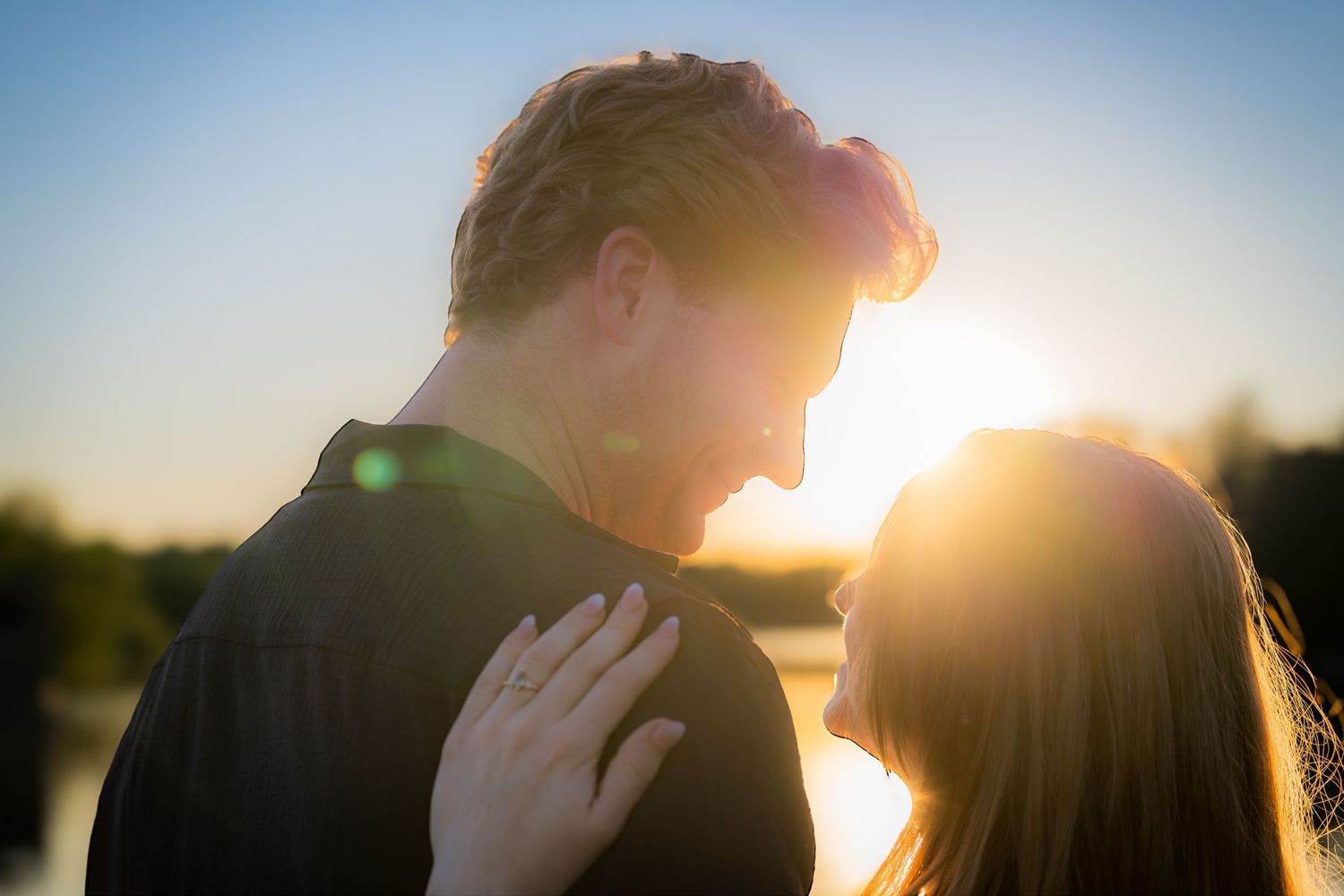 Romantic couple facing each other at golden hour sunset by a lake, bathed in warm glowing light.