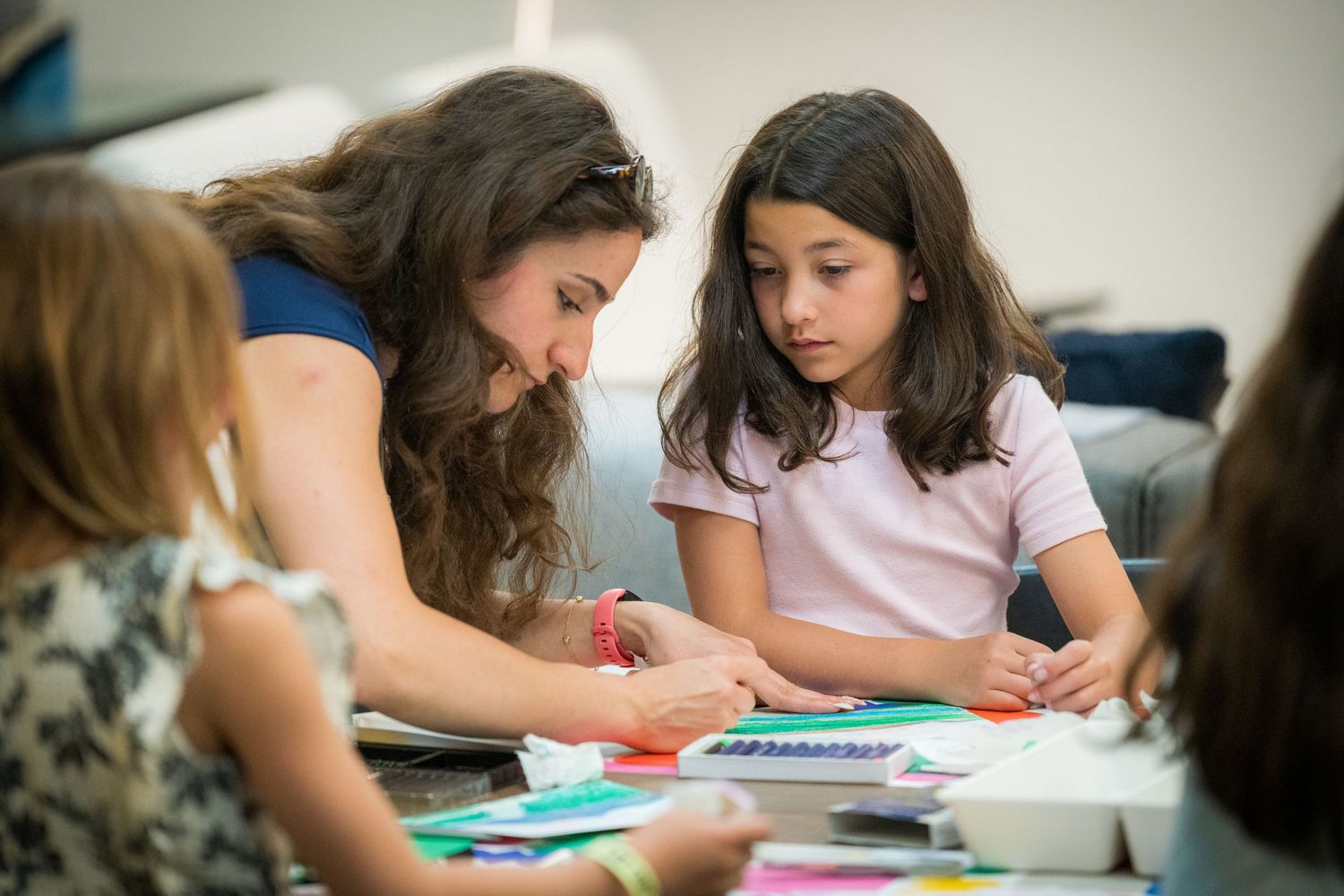 Female teacher assists young girl with colorful paper art project at craft table.