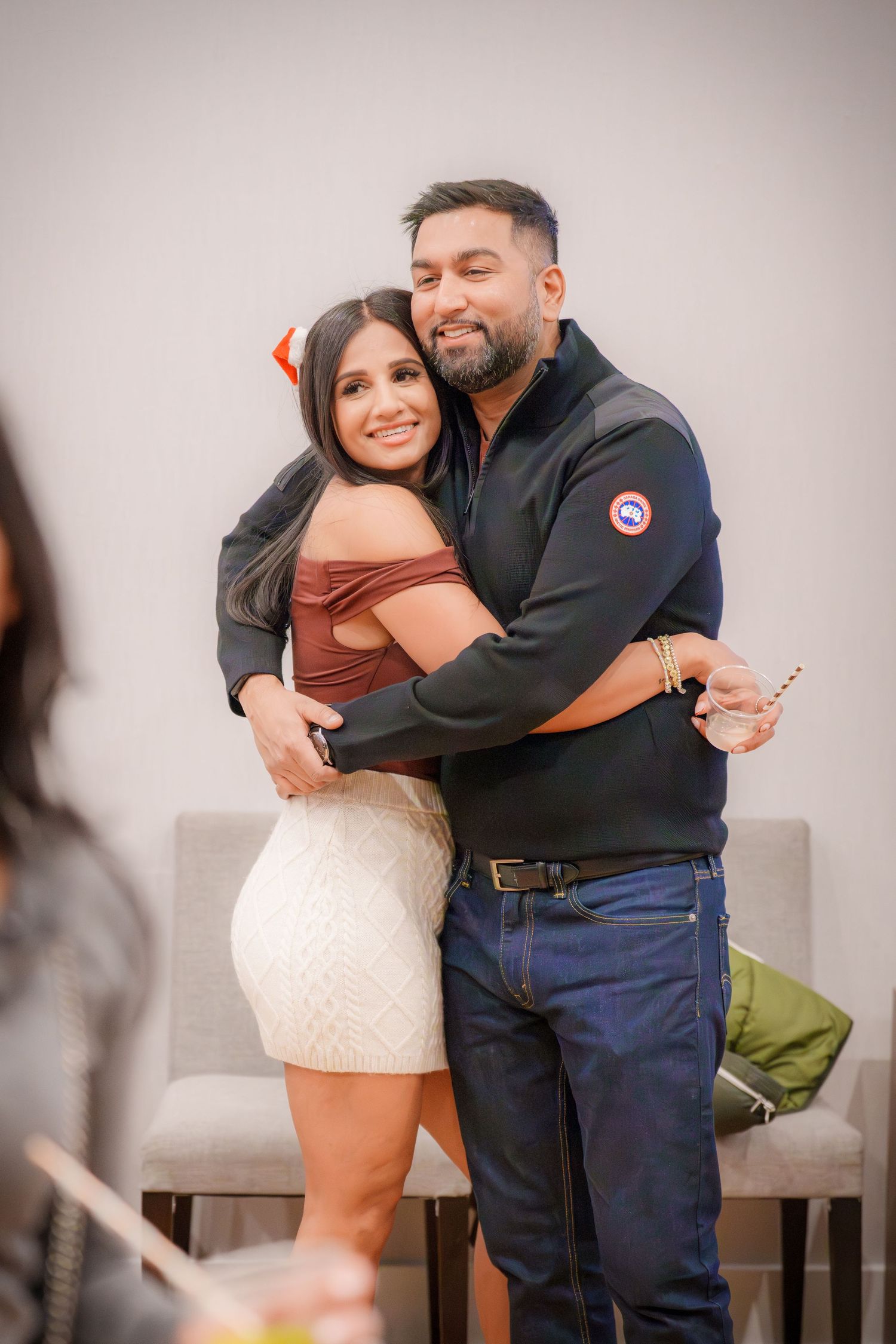 Two people share an affectionate embrace while standing in a room with neutral decor.