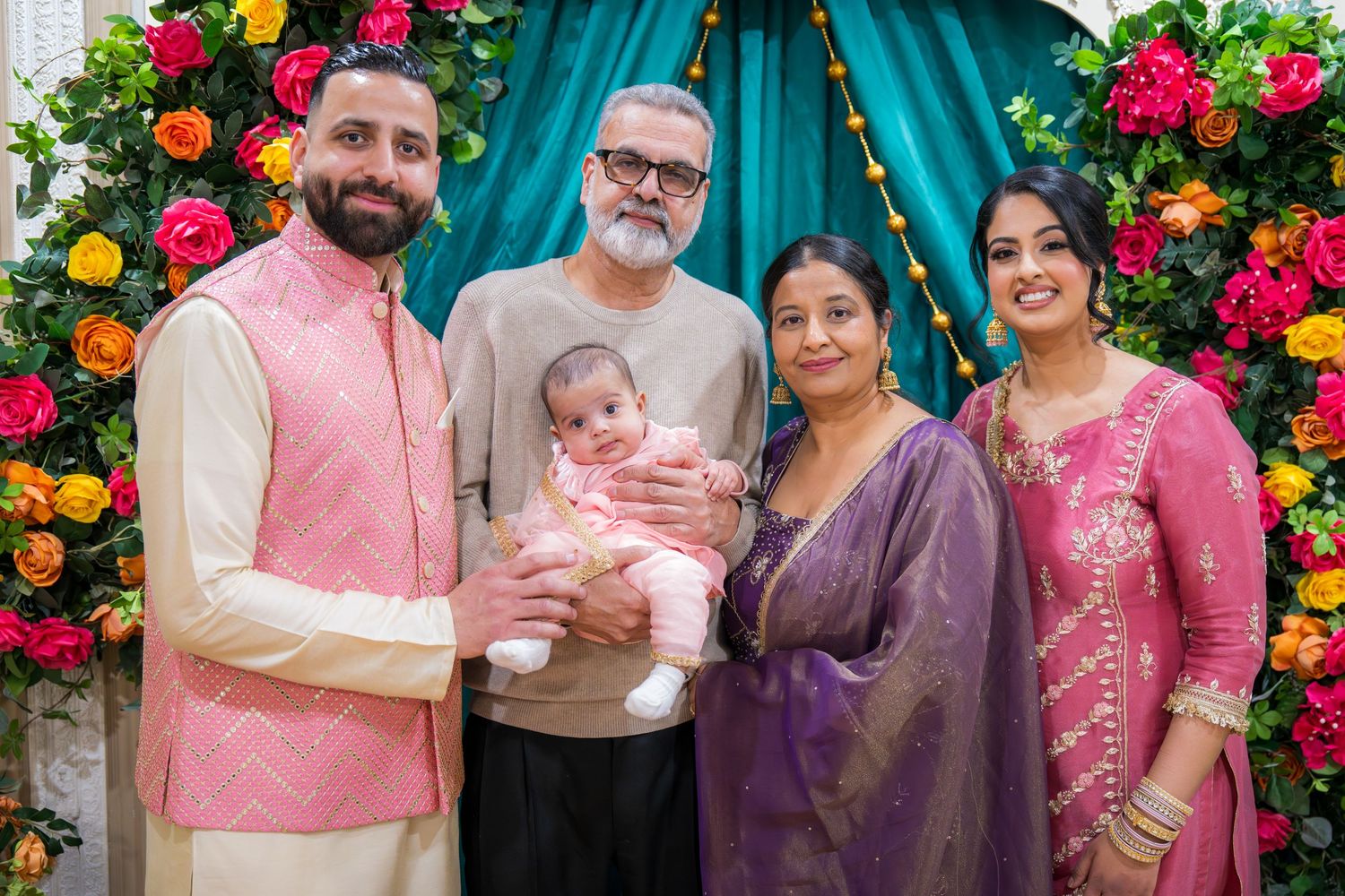 A multigenerational family in festive attire gathers around a newborn baby at a colorful celebration.