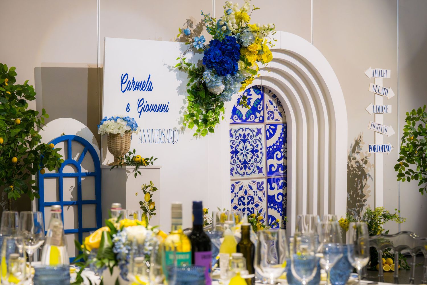 Elegant Italian-themed wedding reception with blue and white arch, floral arrangements, and personalized name sign for Carmela and Giovanni.