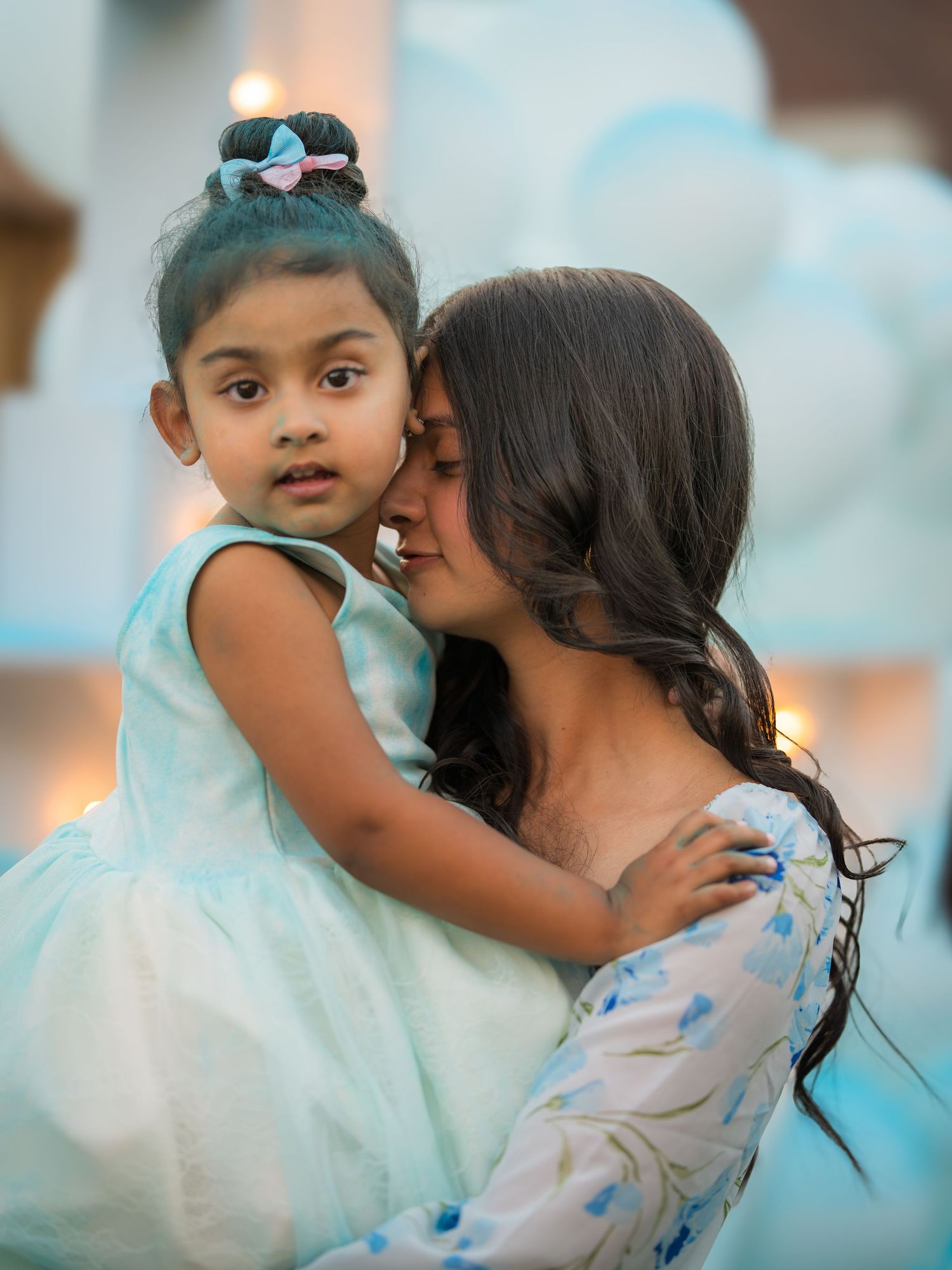Tender moment as a woman kisses a young girl in a light blue tulle dress at a party.