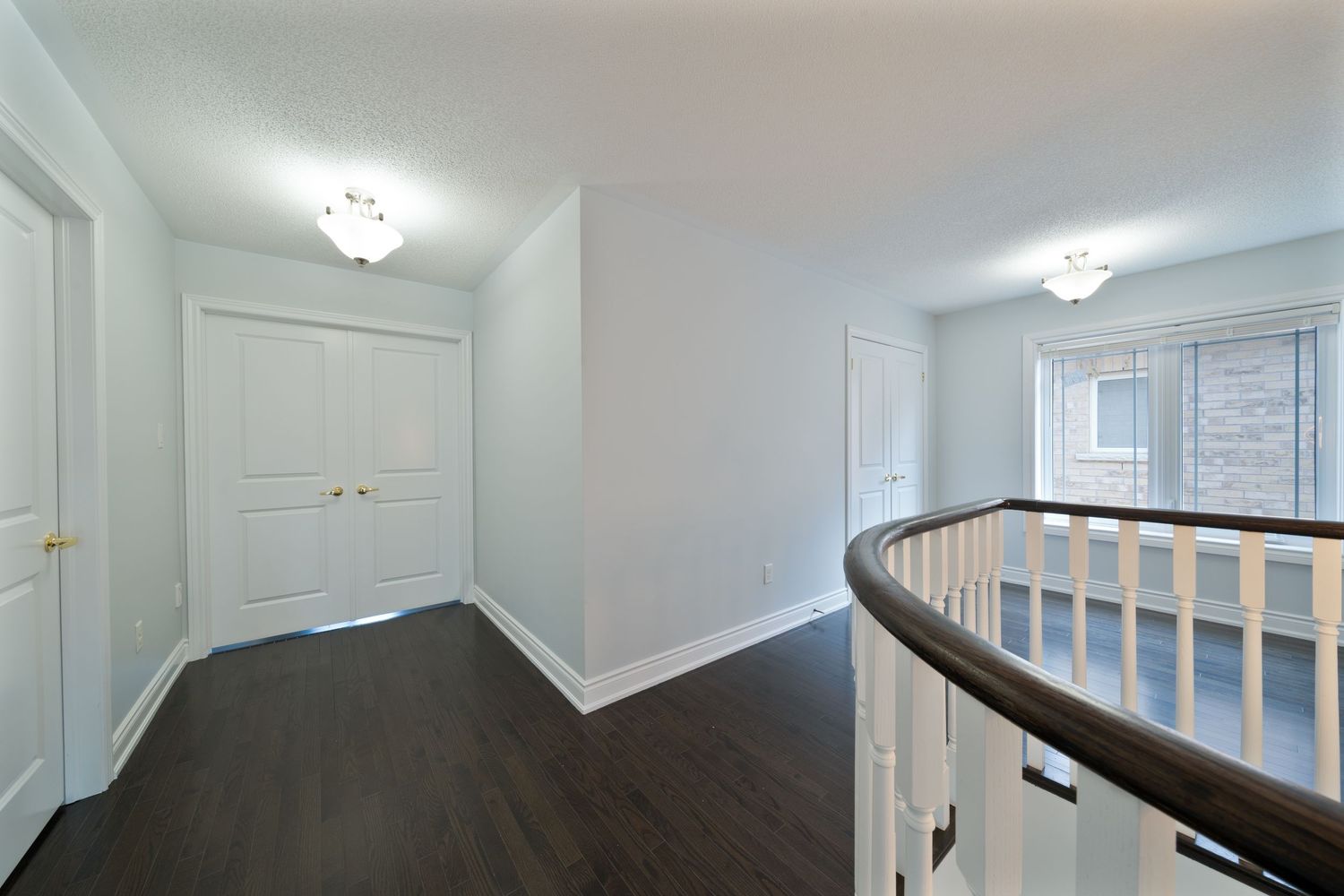 A bright white hallway with crown molding features a curved staircase railing and recessed lighting fixtures.