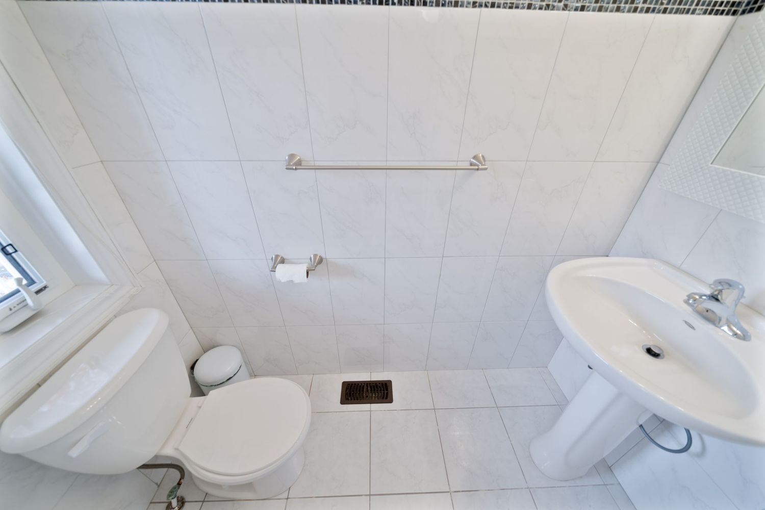 Clean white bathroom interior with toilet, pedestal sink, and tiled floor and walls with towel bar mounted above.
