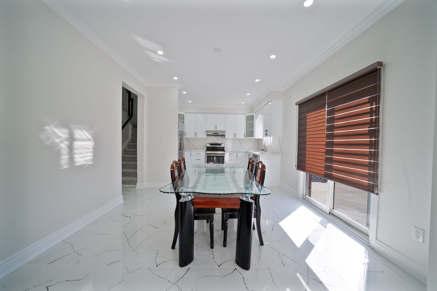 Modern white staircase with wooden steps and glass railings leads to an upper level in a bright minimalist home.