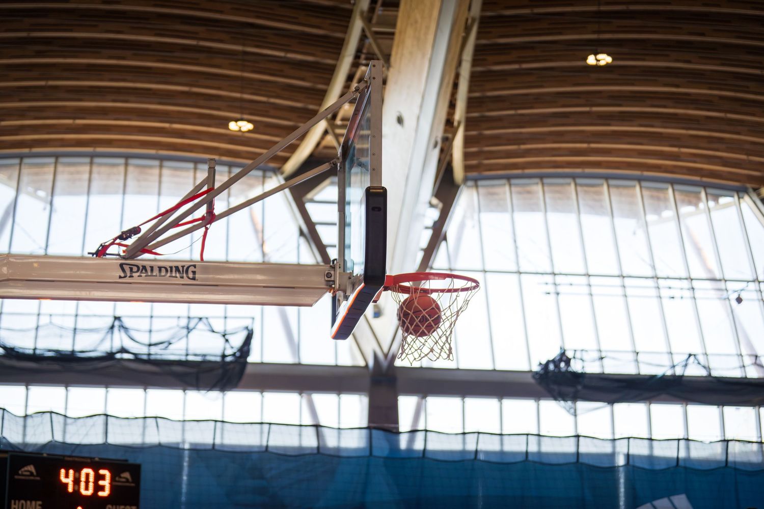 Interior view of a sports arena showing curved wooden beams and netting spanning across the ceiling structure.