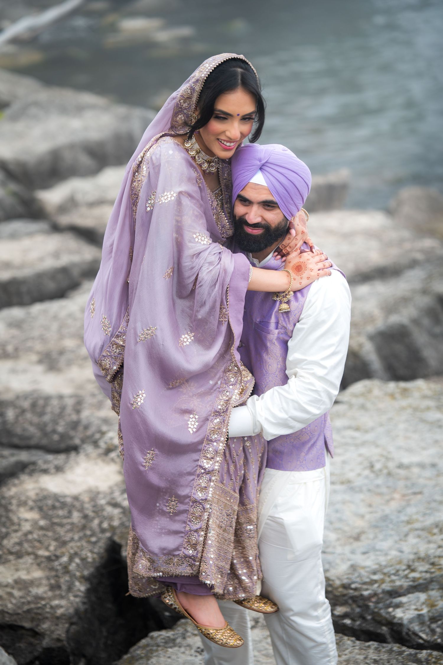 Couple in coordinated purple outfits share tender moments by the water.
