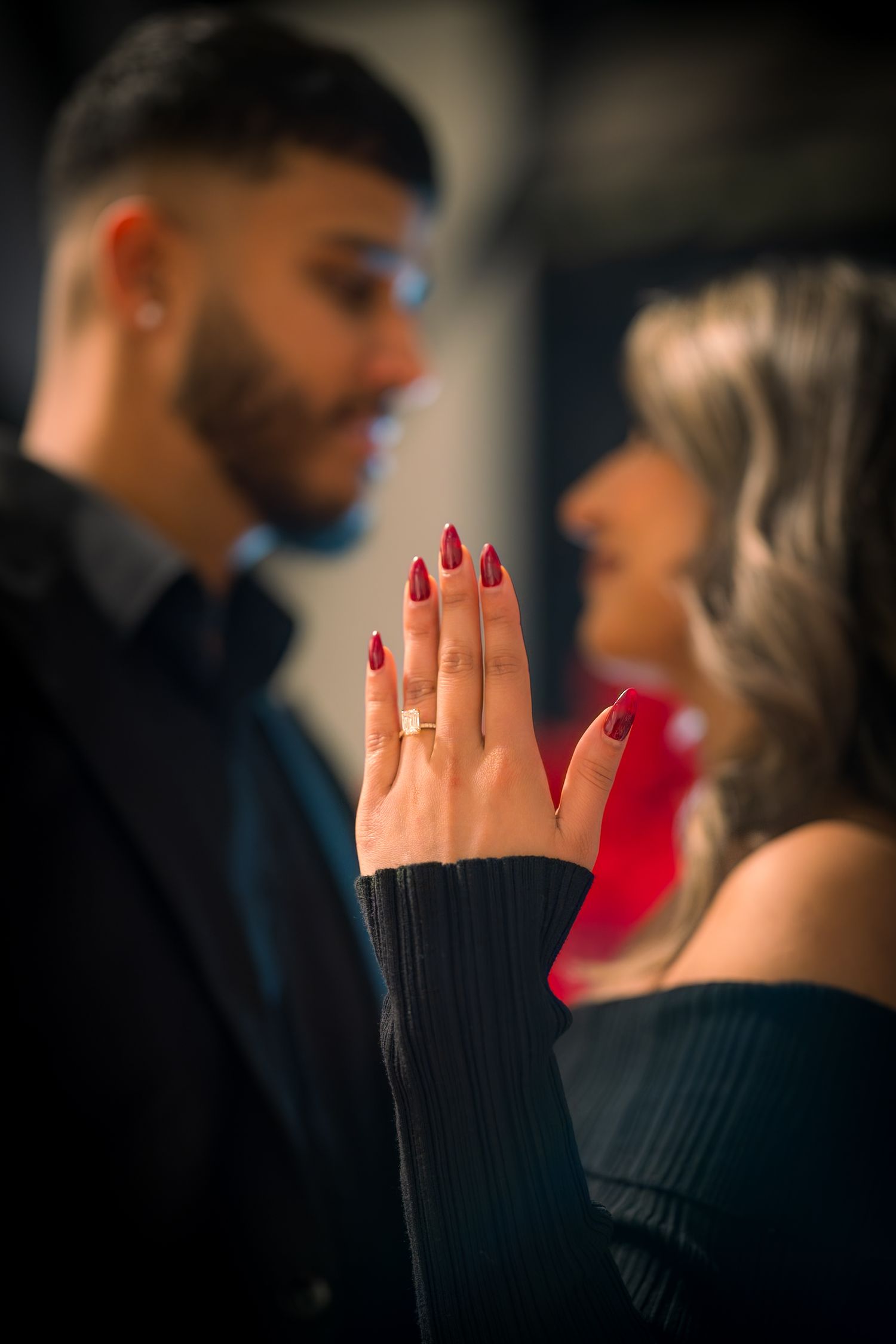 Close-up of hands with red nail polish during an intimate moment against a dark background.