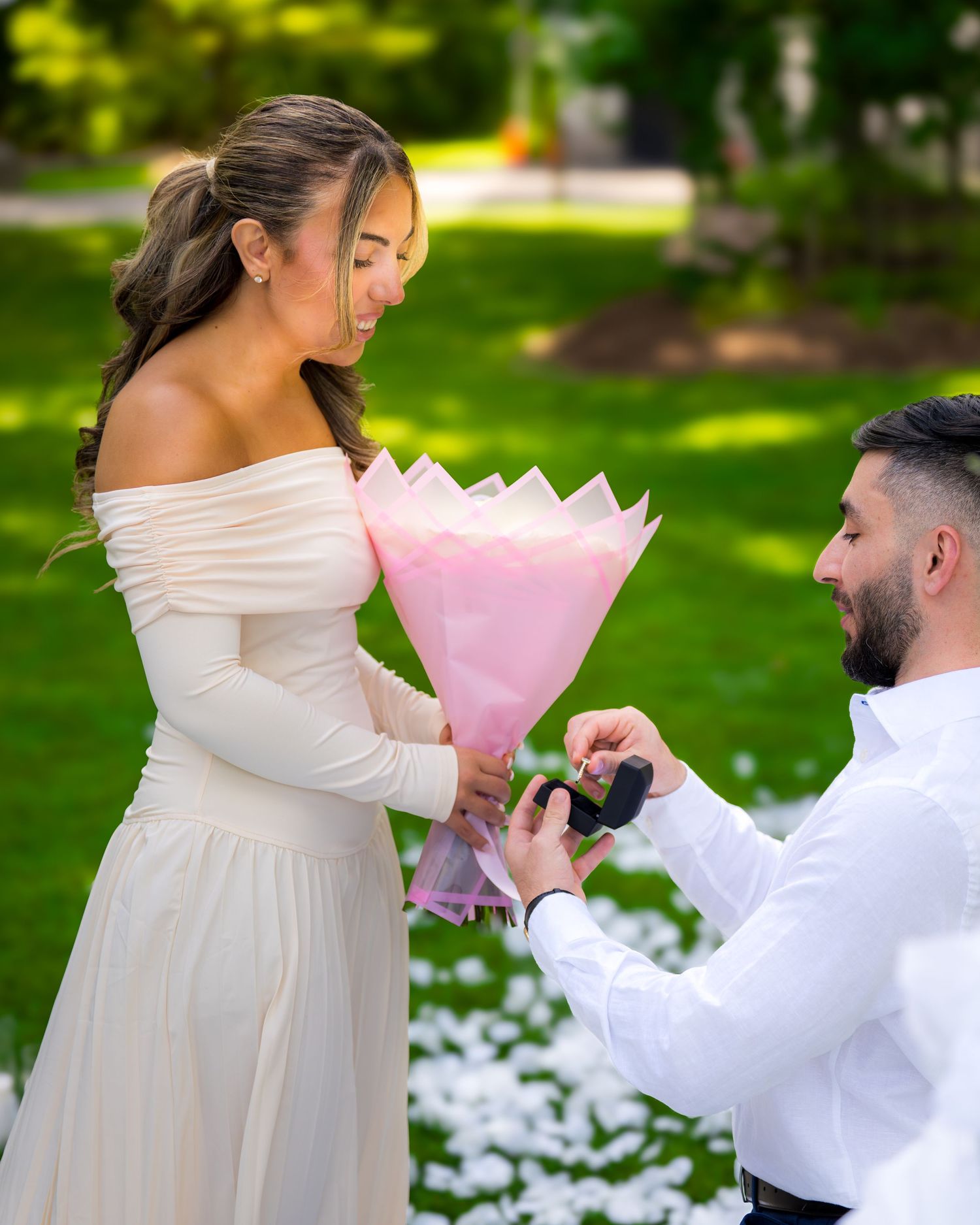 A romantic outdoor proposal scene with pink flowers and white decorations in a garden setting.