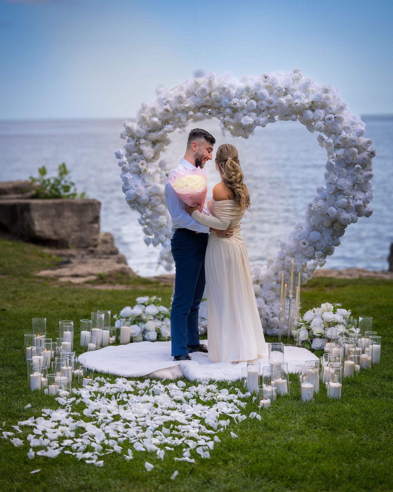 Romantic moment under white balloon arch with scattered petals by waterfront.