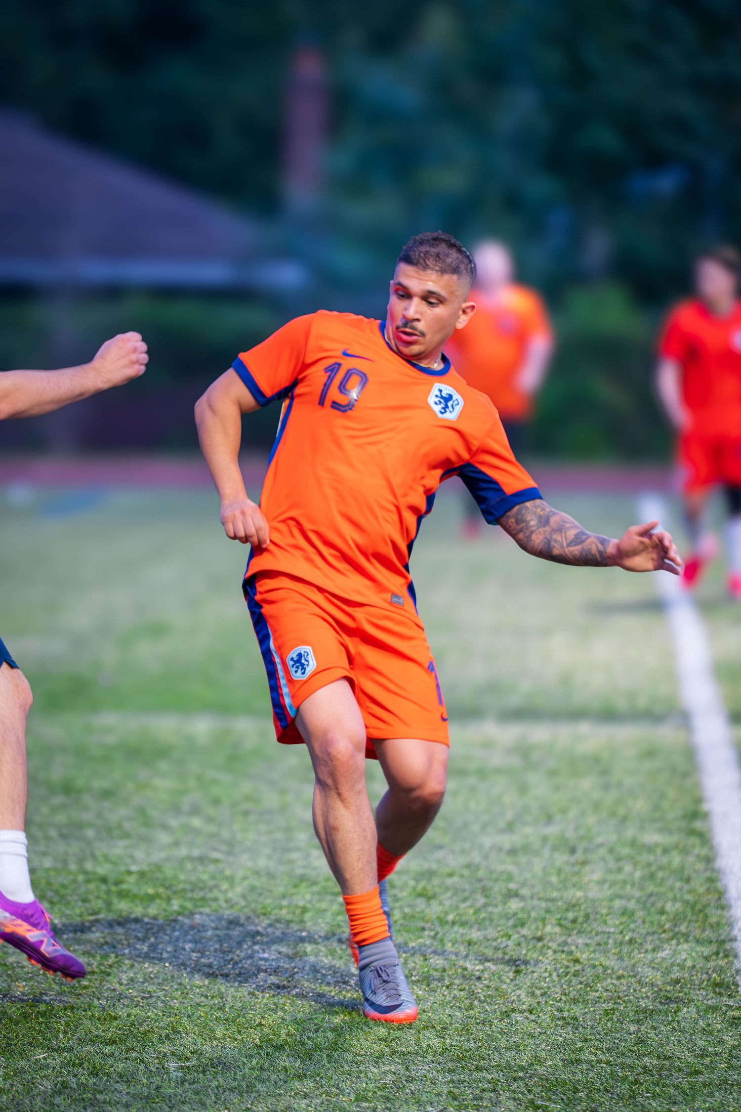 Soccer player in orange jersey stretches to kick ball during intense match on grass field.