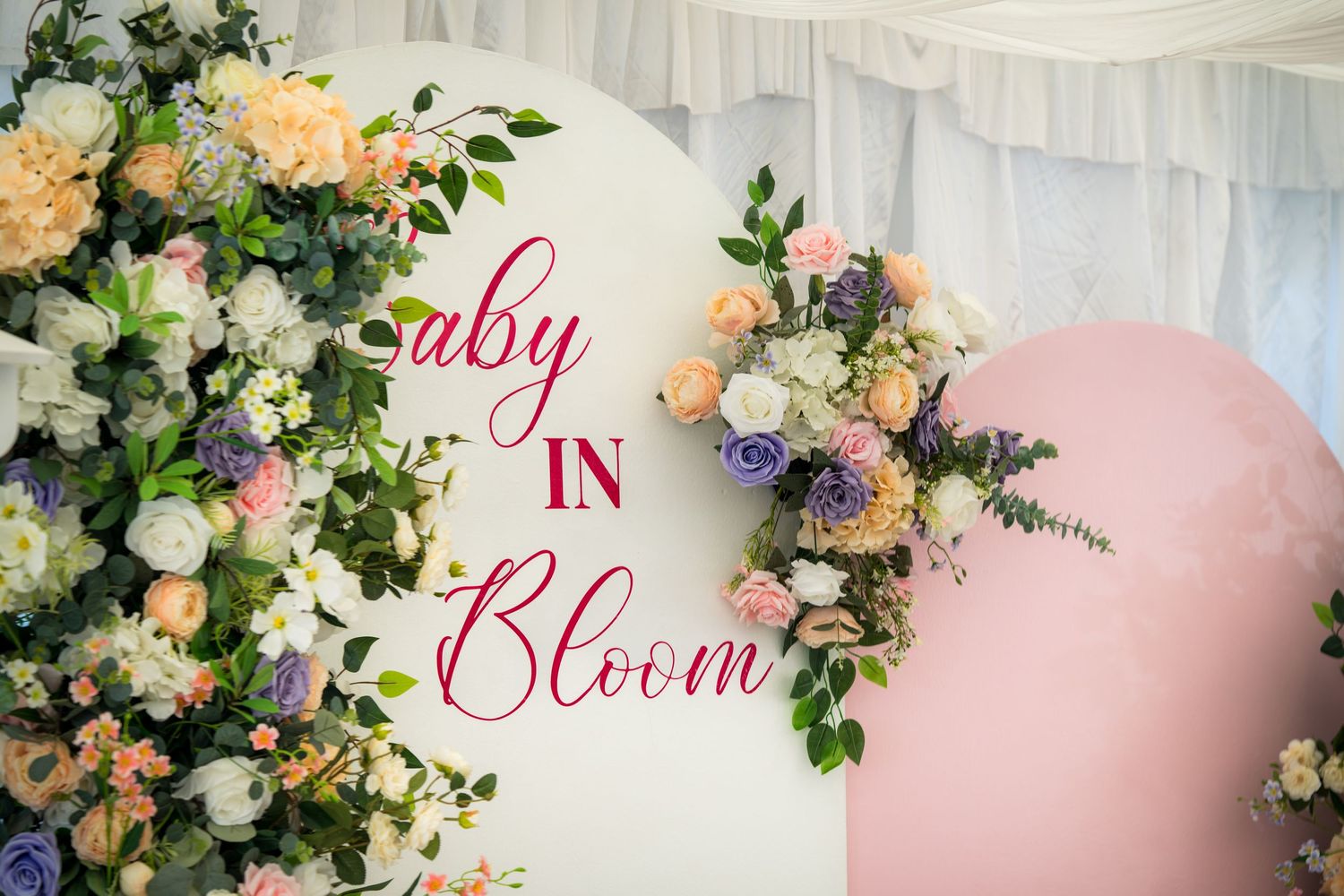 Elegant floral decorations with pink and white flowers adorn a baby shower backdrop with 'Baby Bloom' text.
