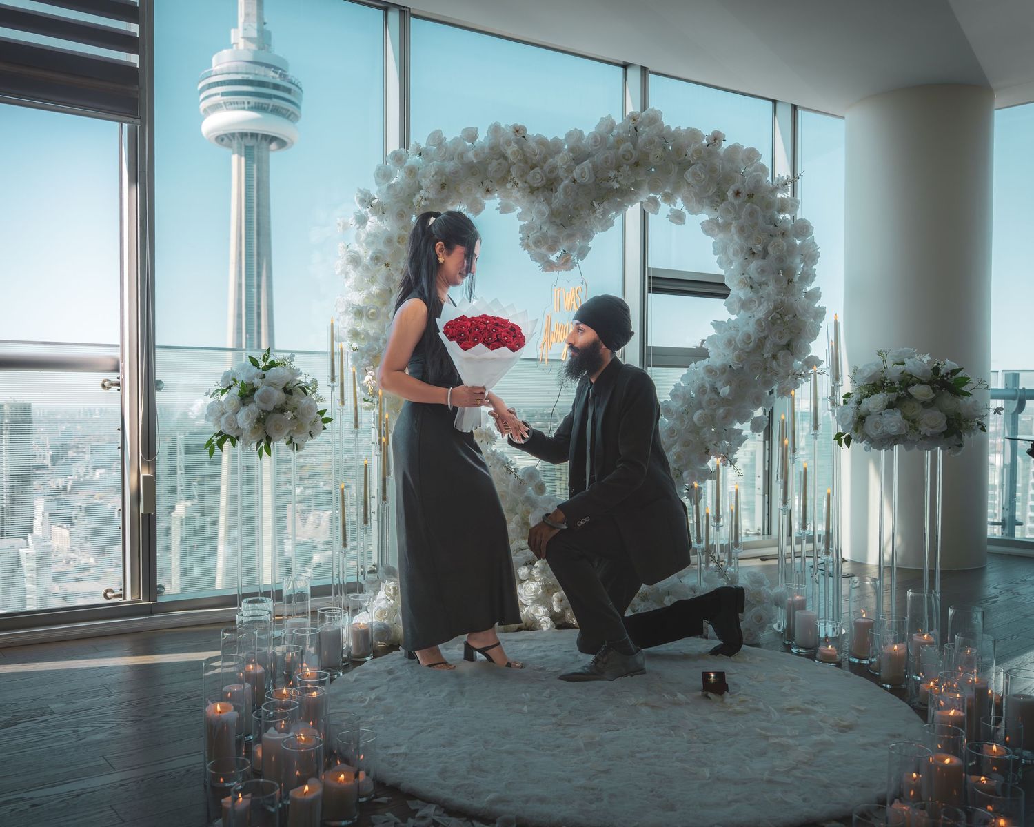 A romantic proposal scene unfolds in a high-rise room with the CN Tower visible through panoramic windows.