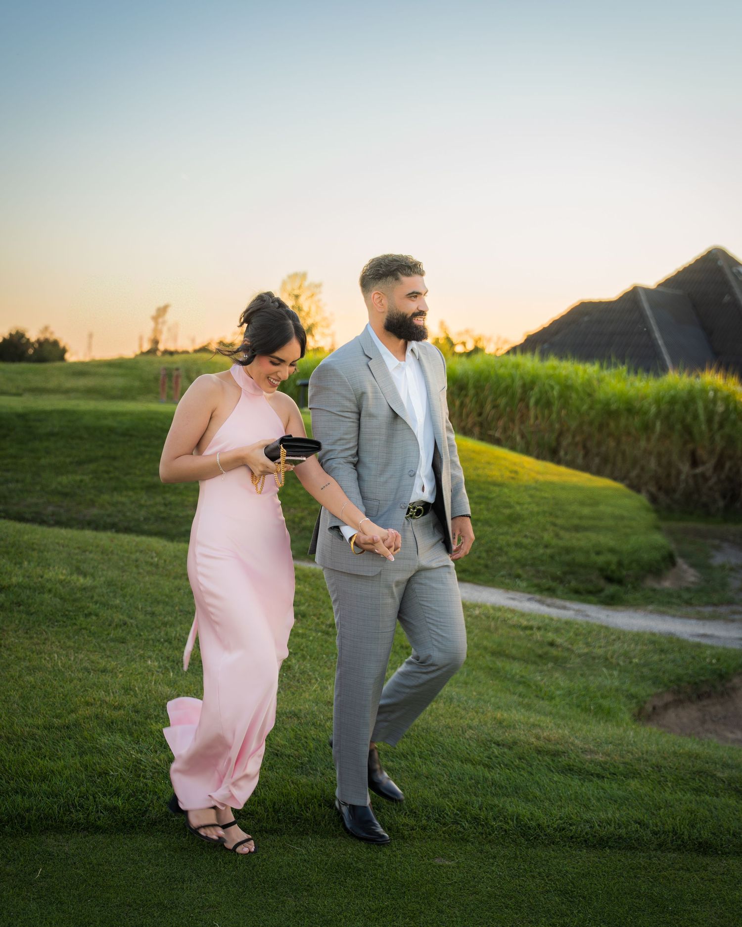 Couple walking together on grassy hill during golden hour photoshoot.