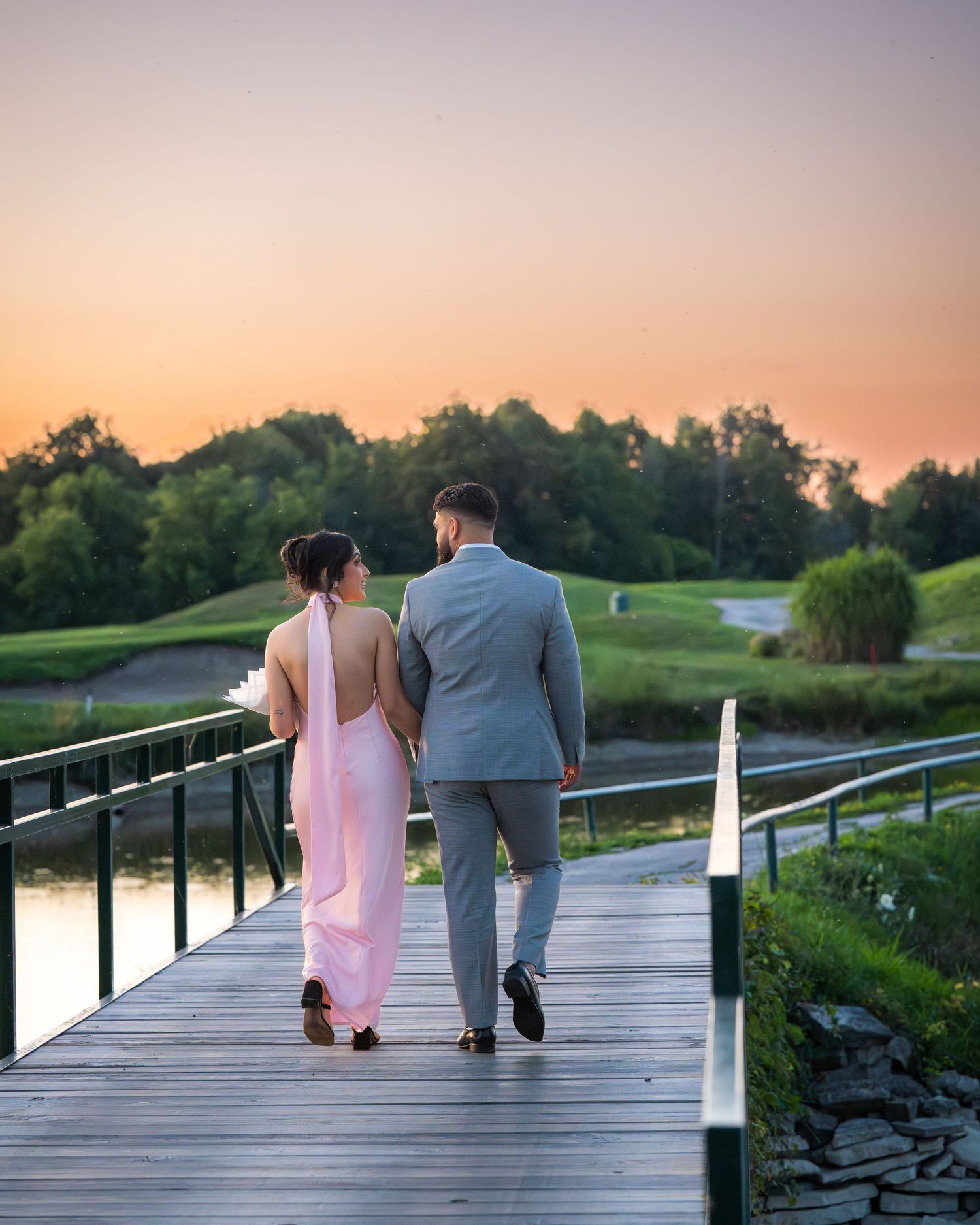 A couple strolls along a wooden boardwalk during a beautiful sunset.