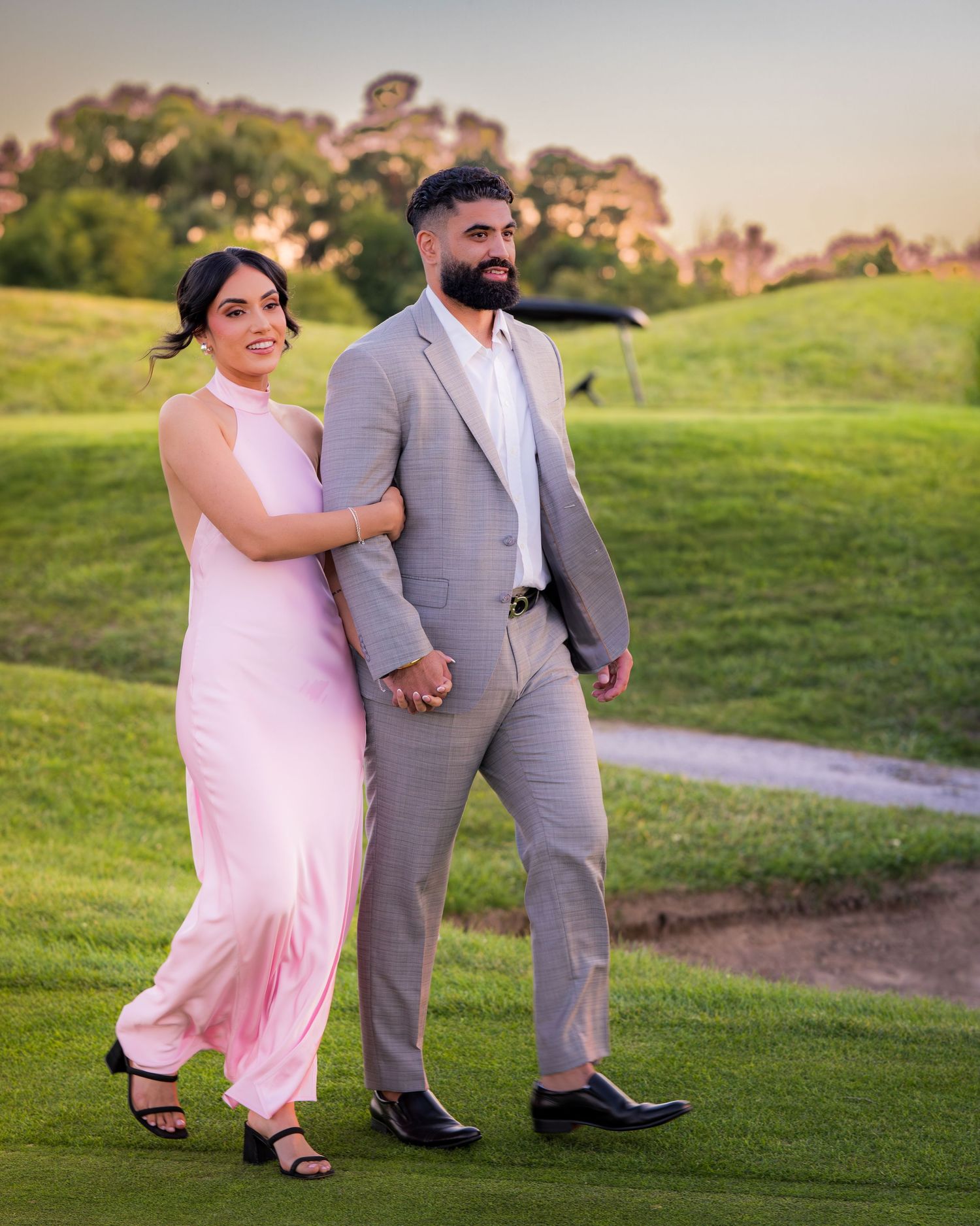 Couple walking together on grassy hill during sunset photoshoot.
