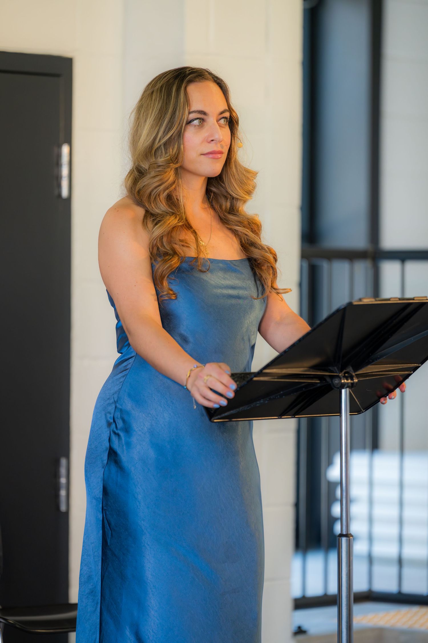 Elegant woman in blue strapless dress stands at music stand during a formal performance event.