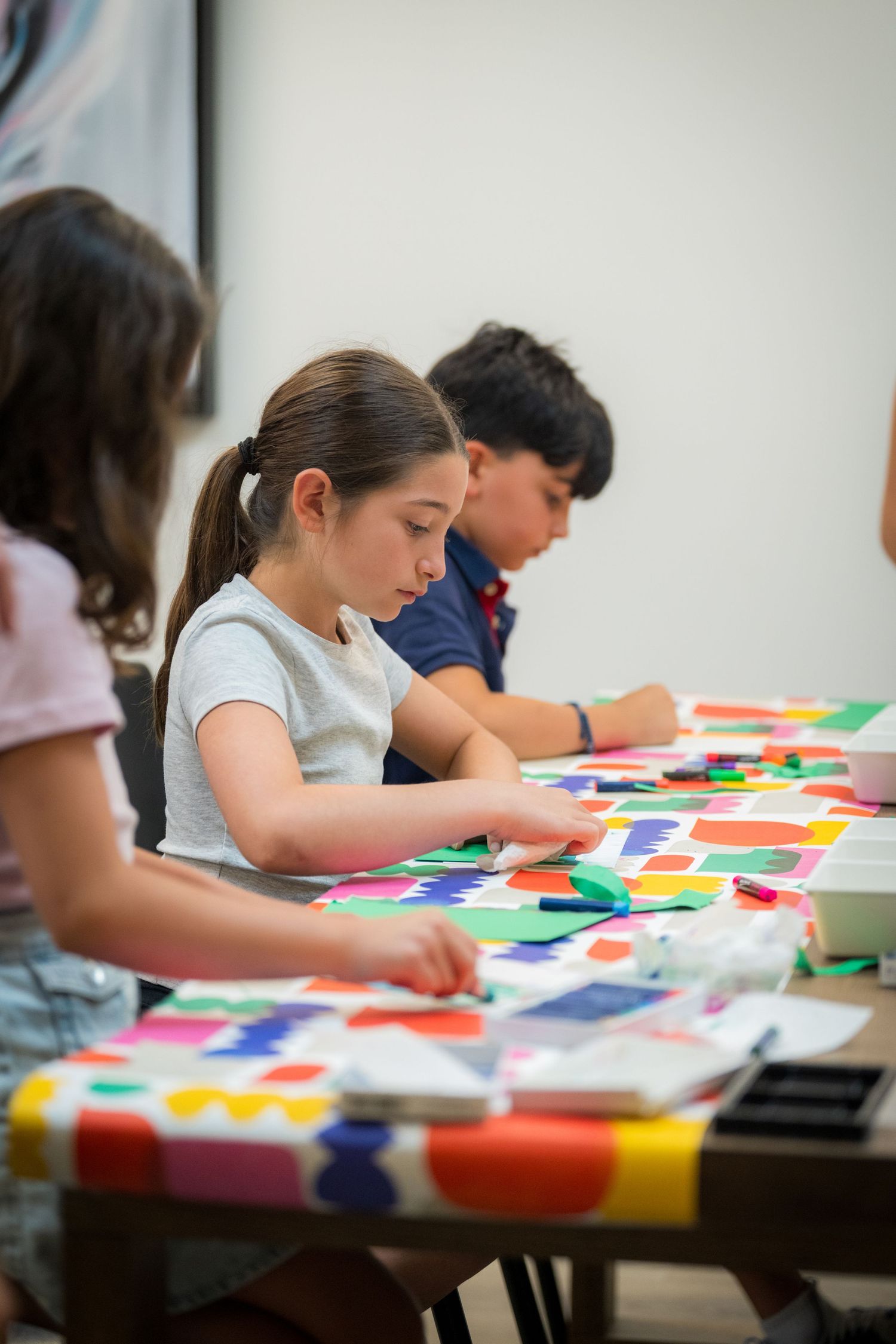 Children engage in a colorful paper collage art activity at a table covered with vibrant cut shapes.