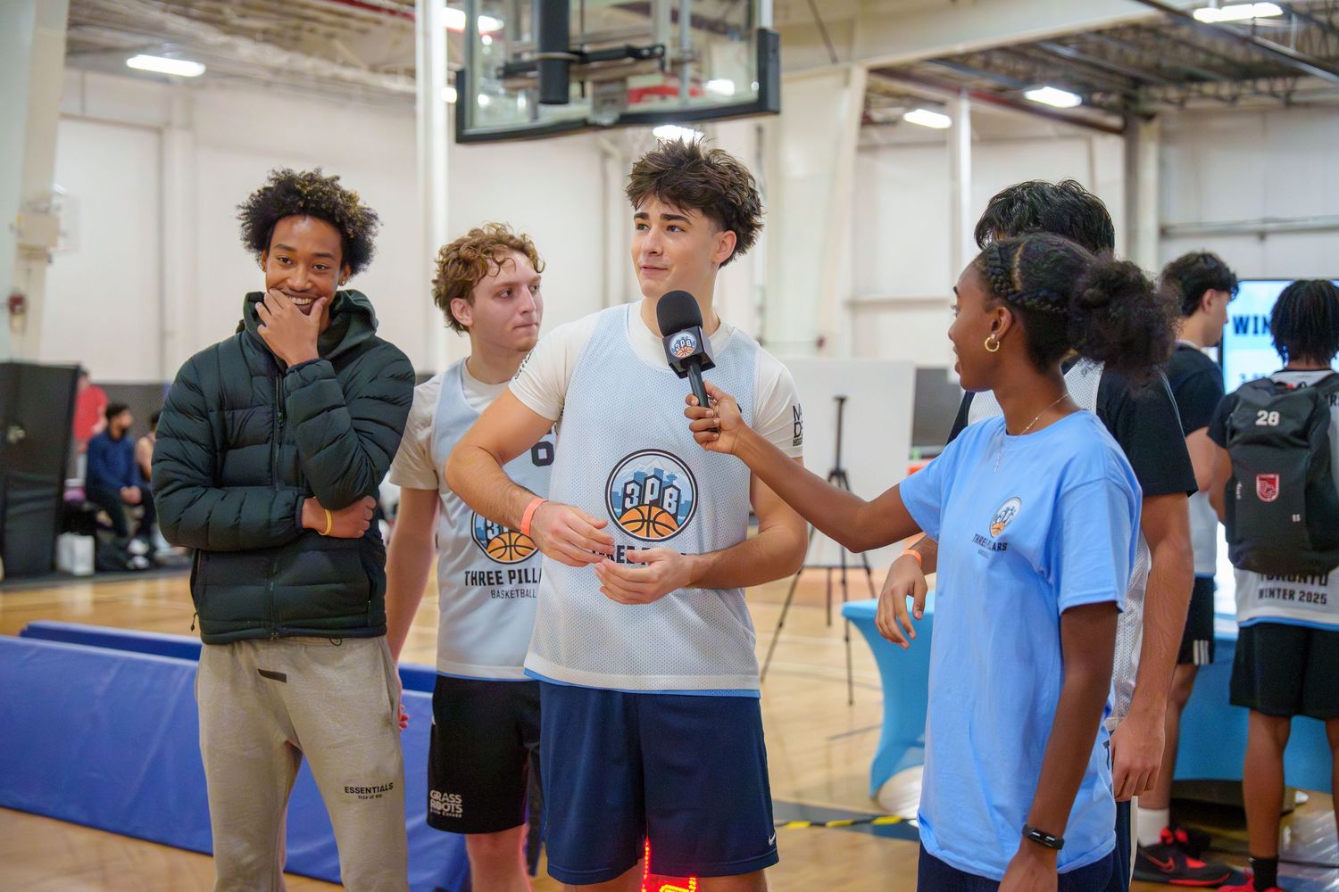 Teen basketball players being interviewed with a microphone at an indoor sports event on a gymnasium court.