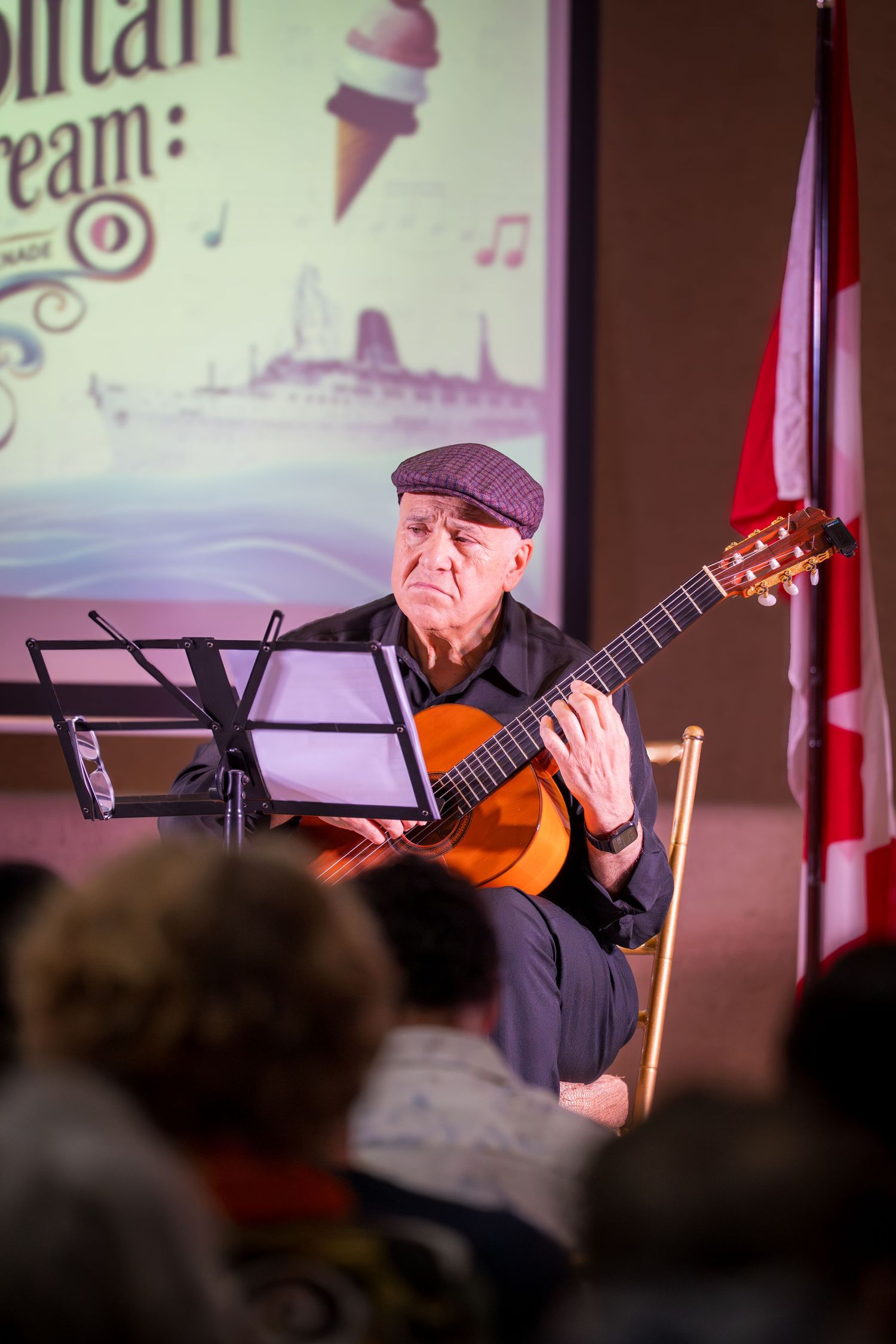 Elderly man playing classical guitar while reading sheet music at an indoor performance event.