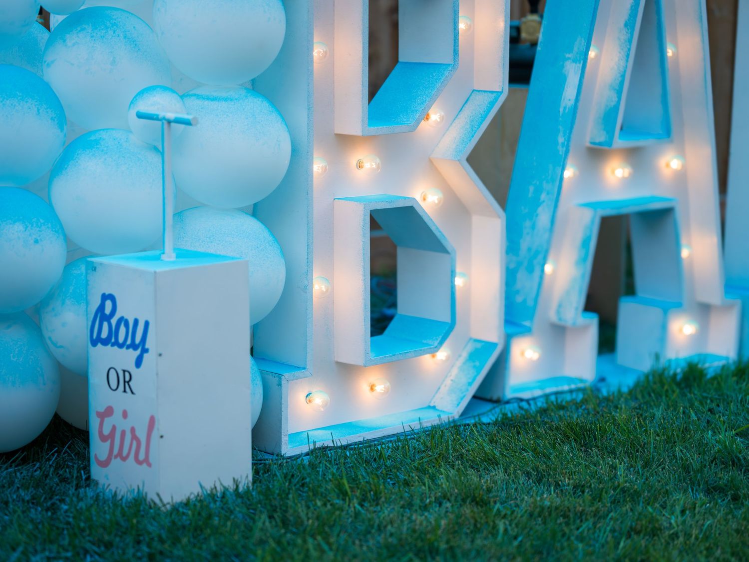 Gender reveal party setup with lit marquee BA letters, blue balloons, and a Boy or Girl box.