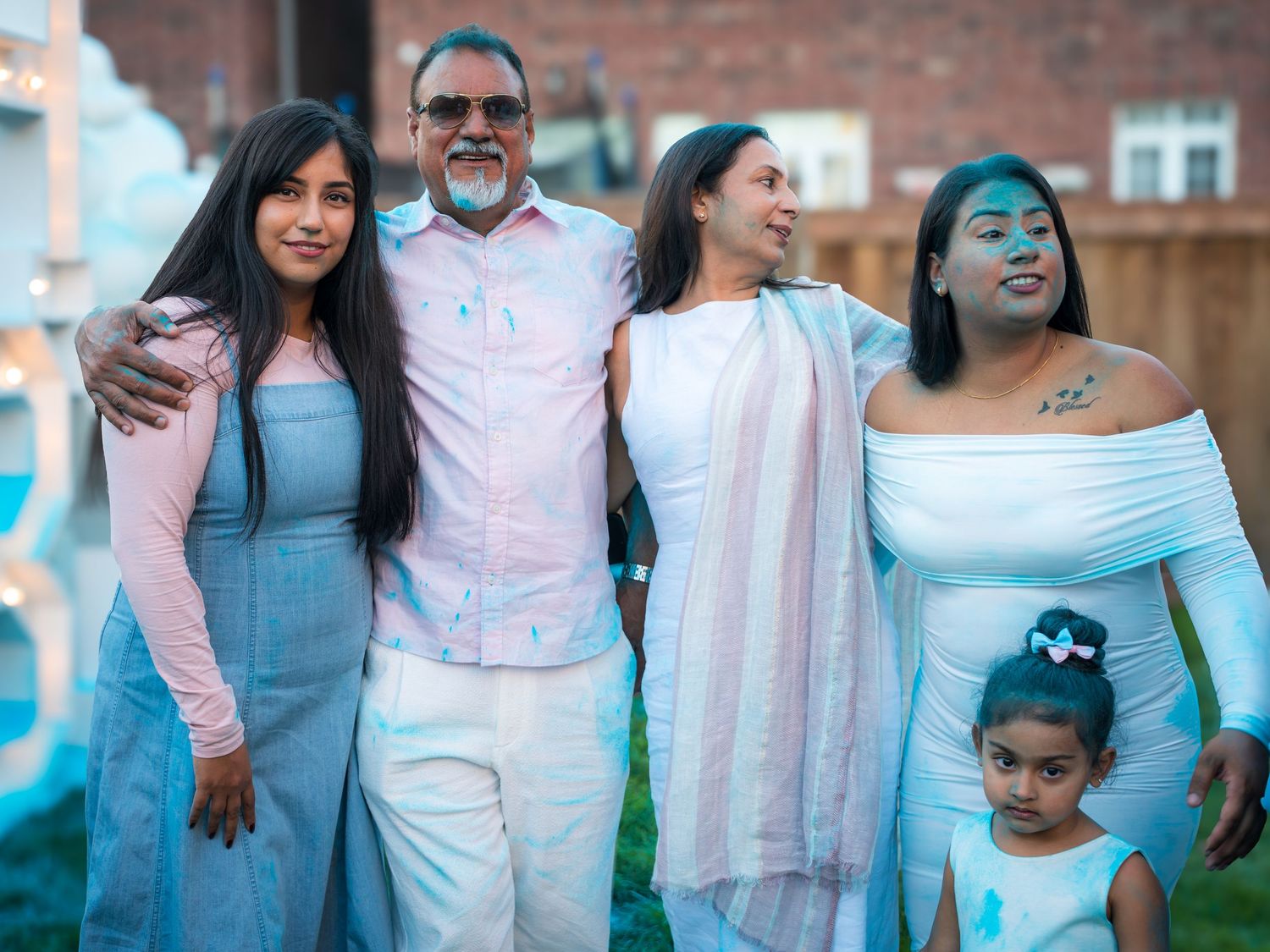 Family of five in blue and white outfits smile together at an outdoor gender reveal party at dusk.