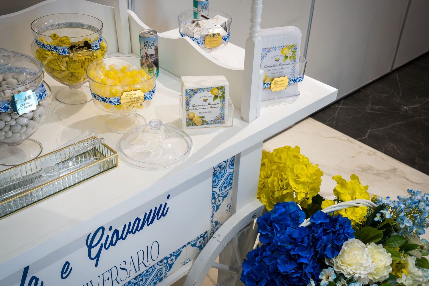 Italian-themed wedding candy bar with lemon treats, blue tile accents, and colorful floral decorations.