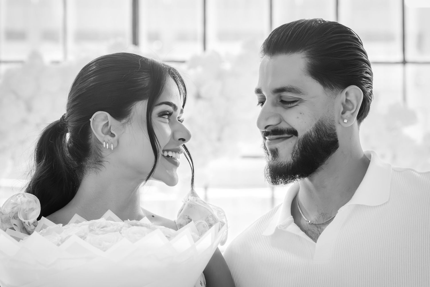 Black and white portrait of smiling couple gazing at each other during romantic proposal moment.