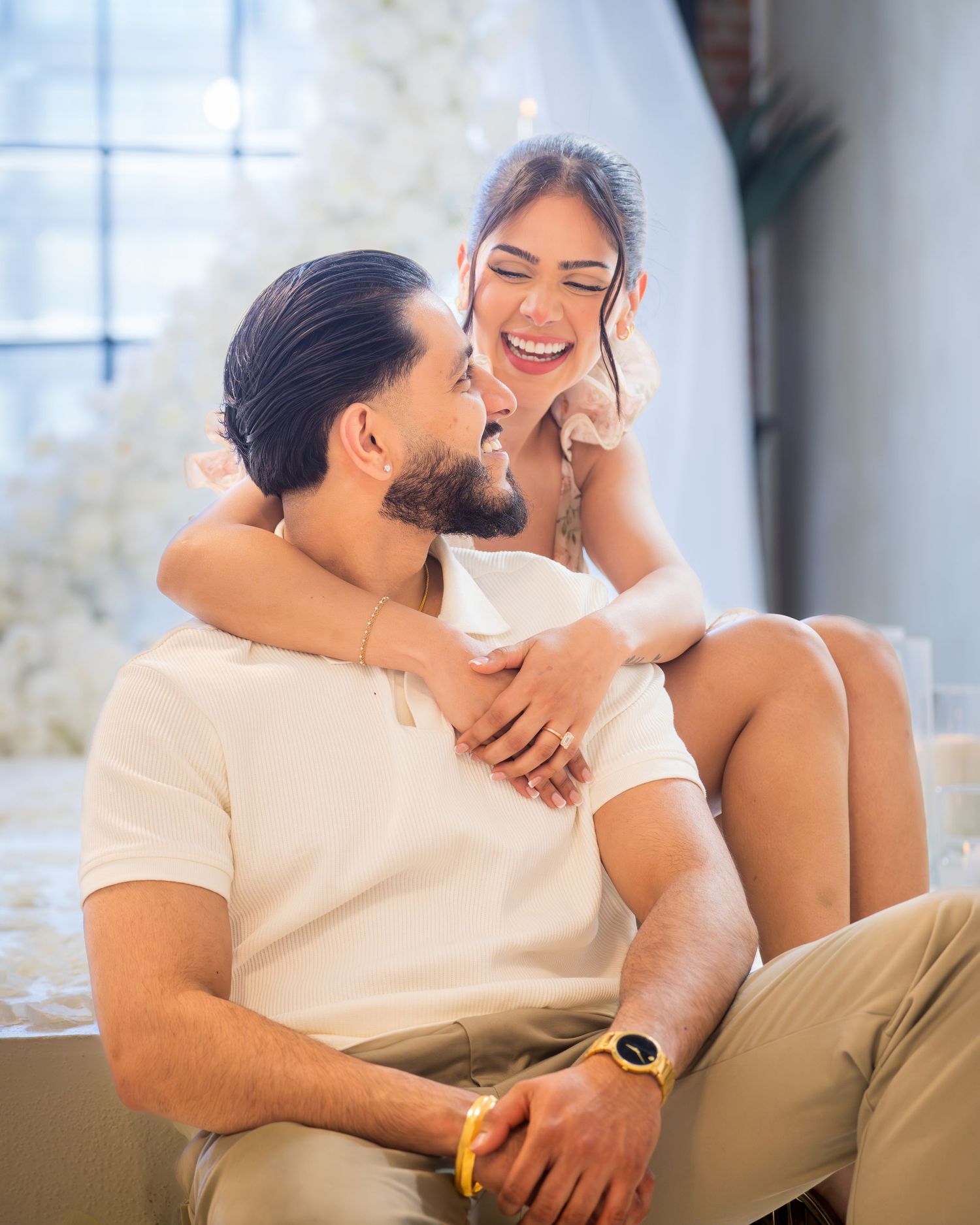 Happy couple sitting together laughing, woman embracing man from behind in bright decorated space.