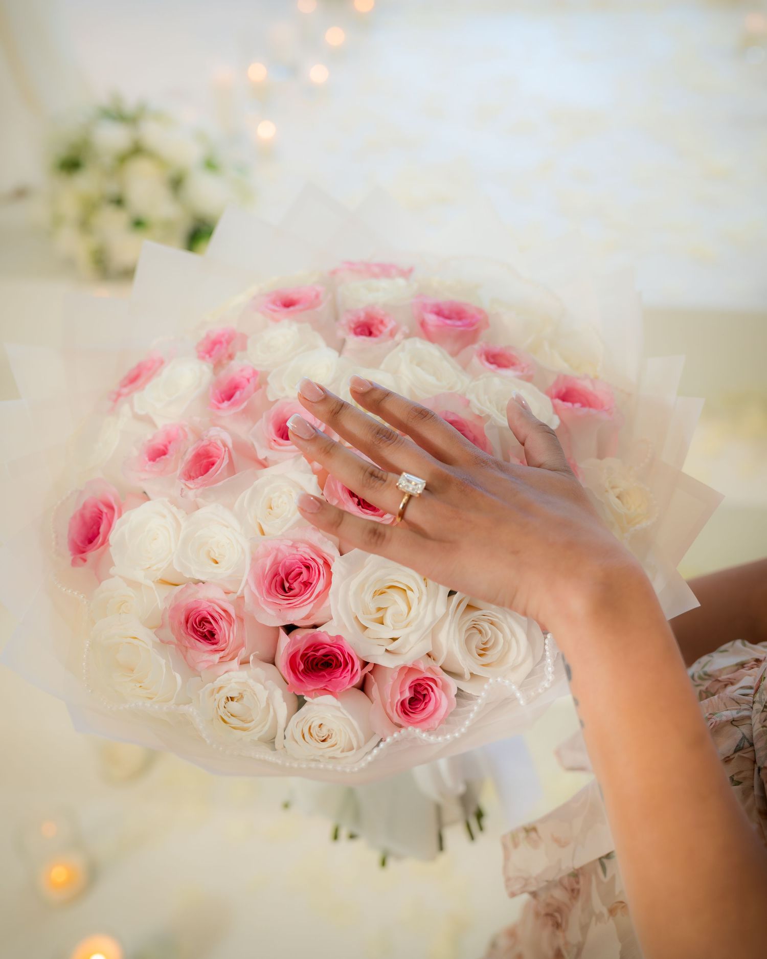 Close-up of engagement ring on hand resting over a bouquet of pink and white roses.
