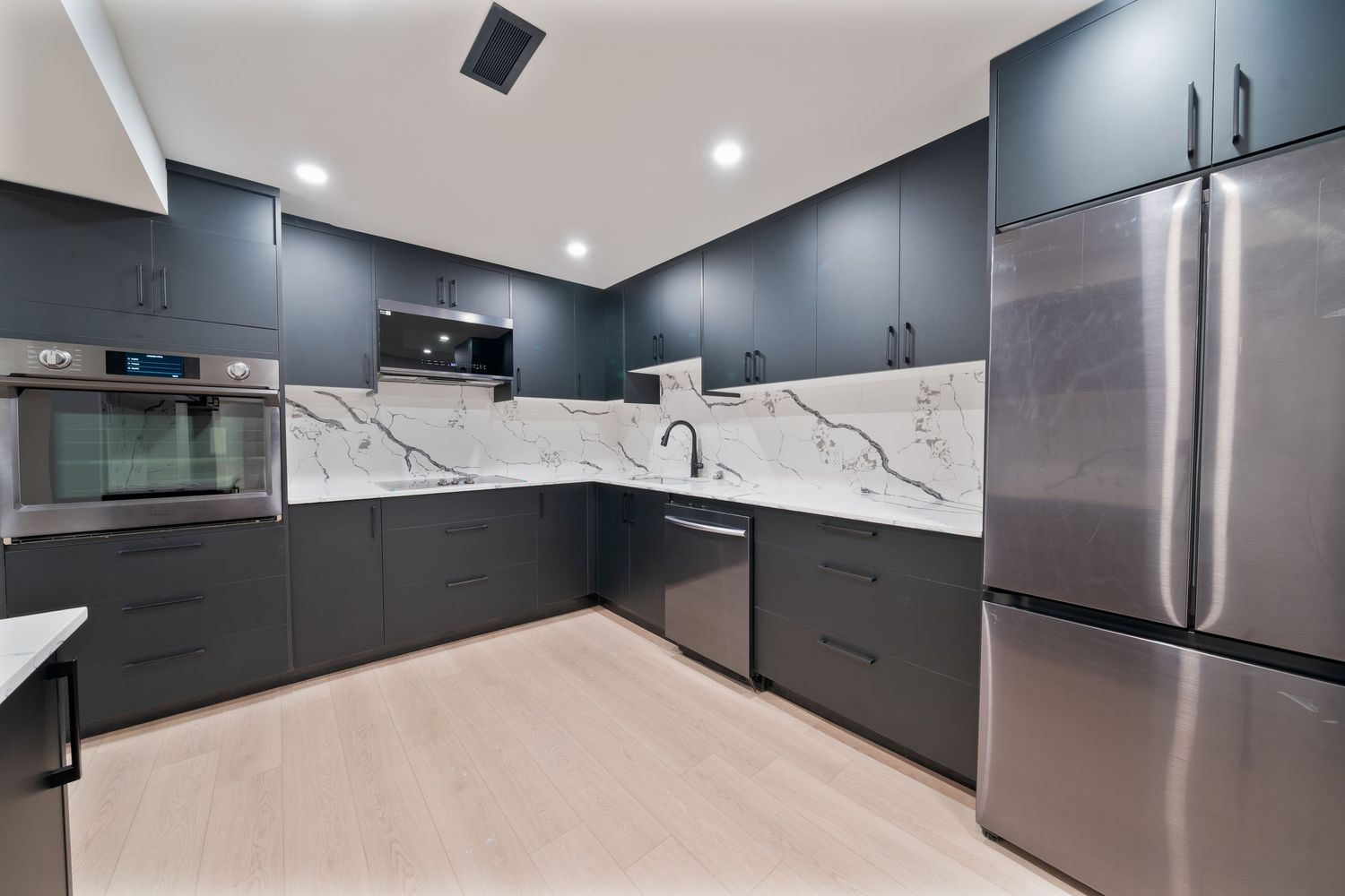 Modern kitchen features dark gray cabinets, stainless steel appliances, and white marble backsplash in an open layout design.