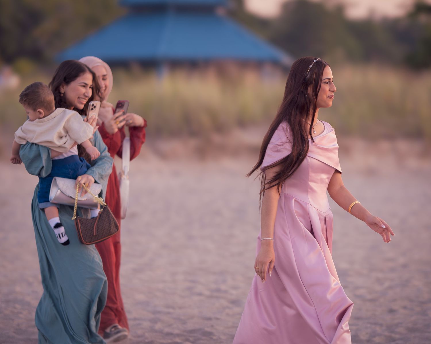 A couple in pink and blue outfits dances playfully together on a sandy beach at sunset.