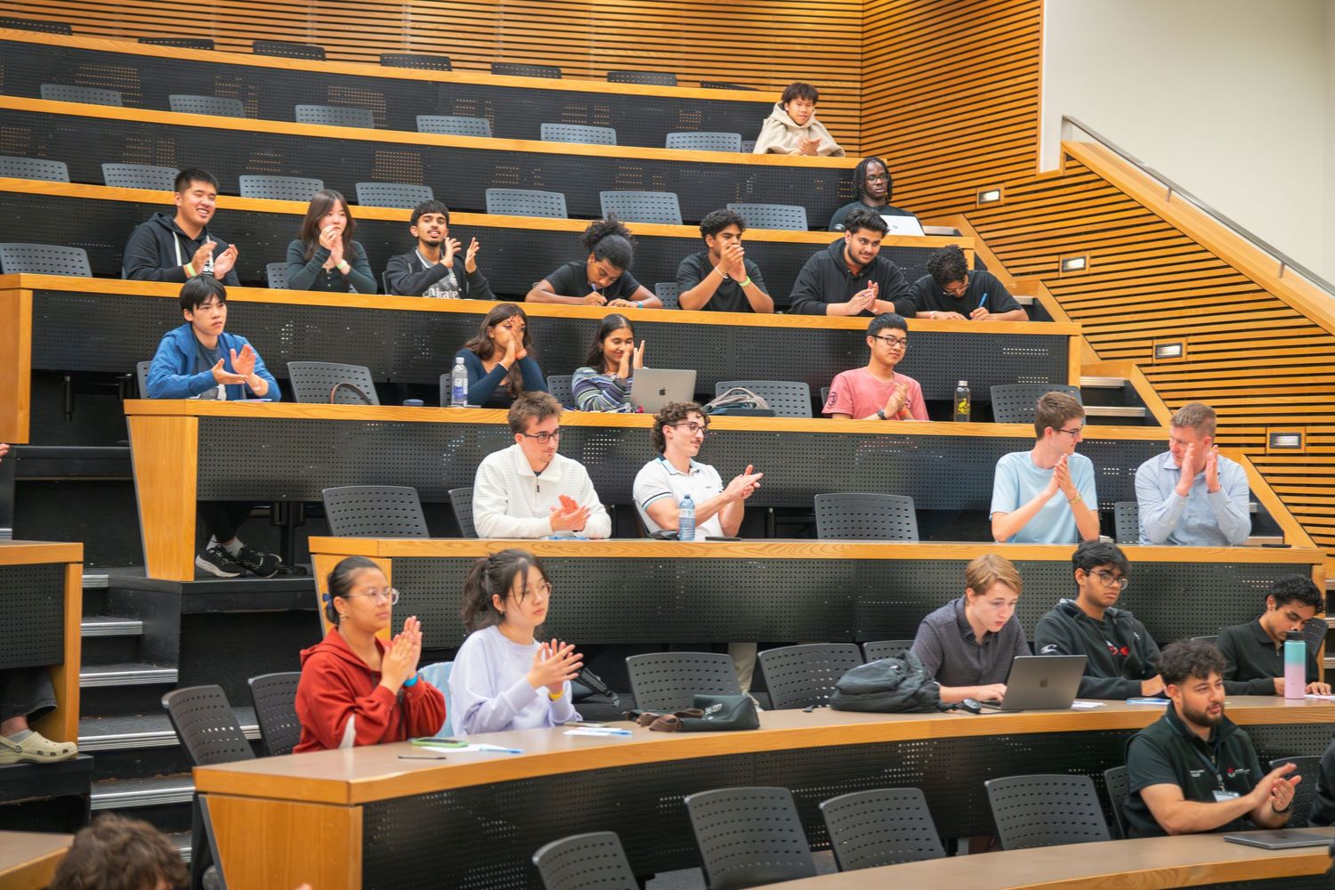 Students seated in tiered lecture hall rows during an academic presentation.