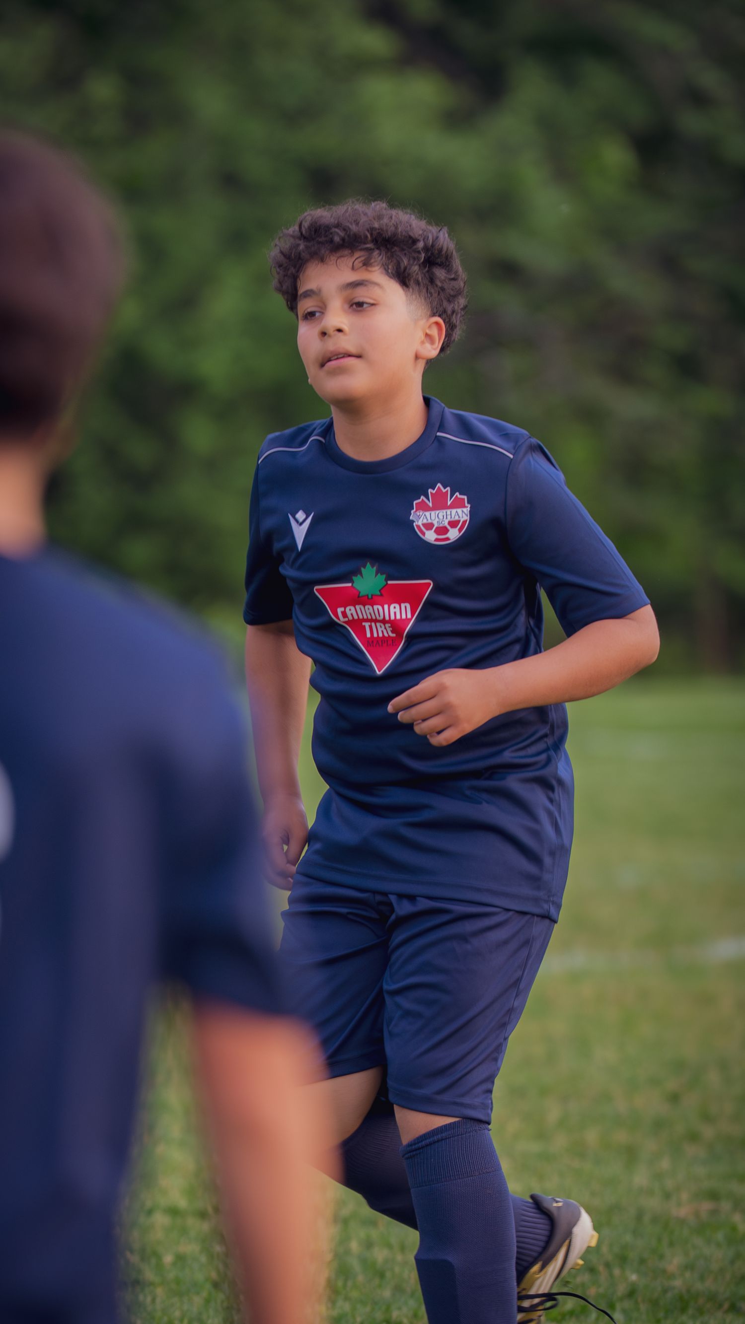 A young soccer player in a navy blue uniform stretches and warms up on a grassy field during practice.