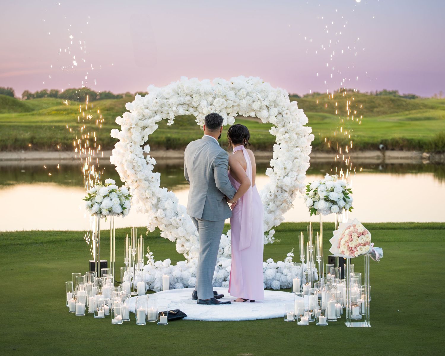 An elegant outdoor wedding ceremony setup with white floral arches on a lush golf course at sunset.