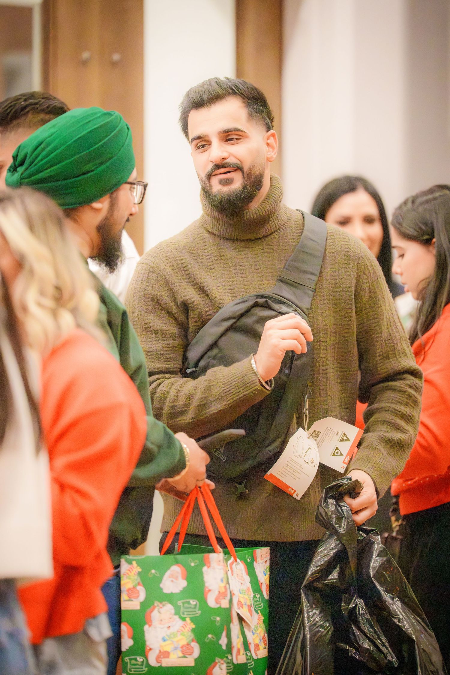 People at a holiday gathering hold festive shopping bags and gifts.
