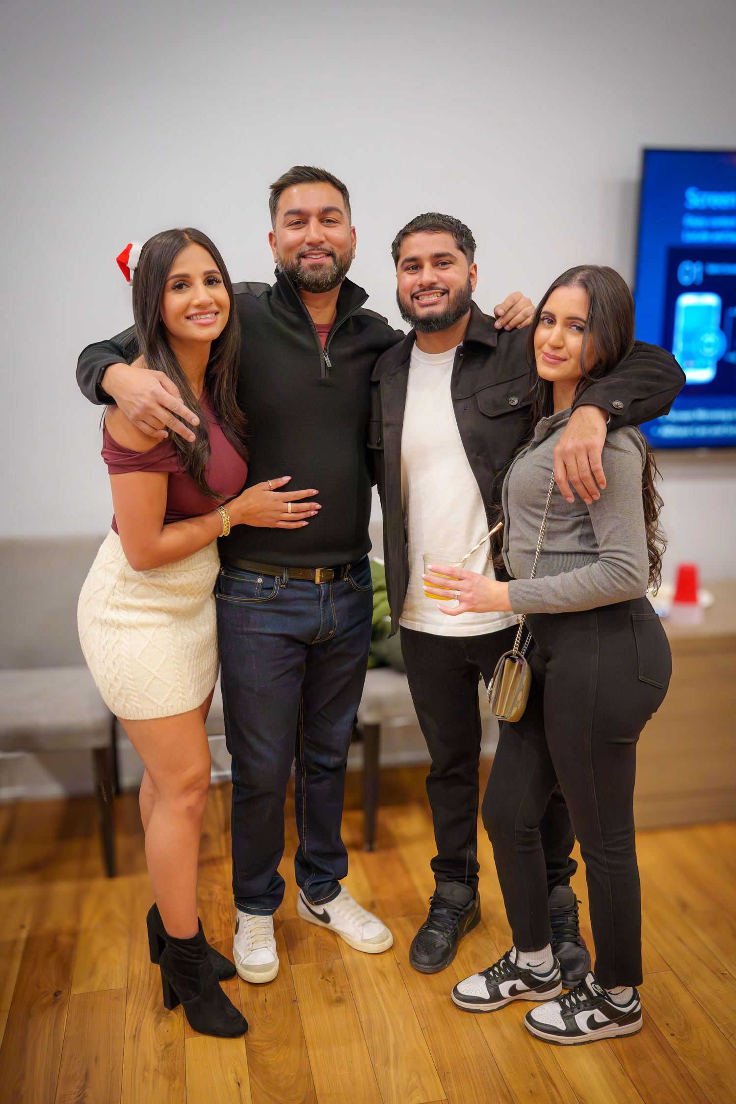 Group of friends posing together on a wooden floor at an indoor gathering.