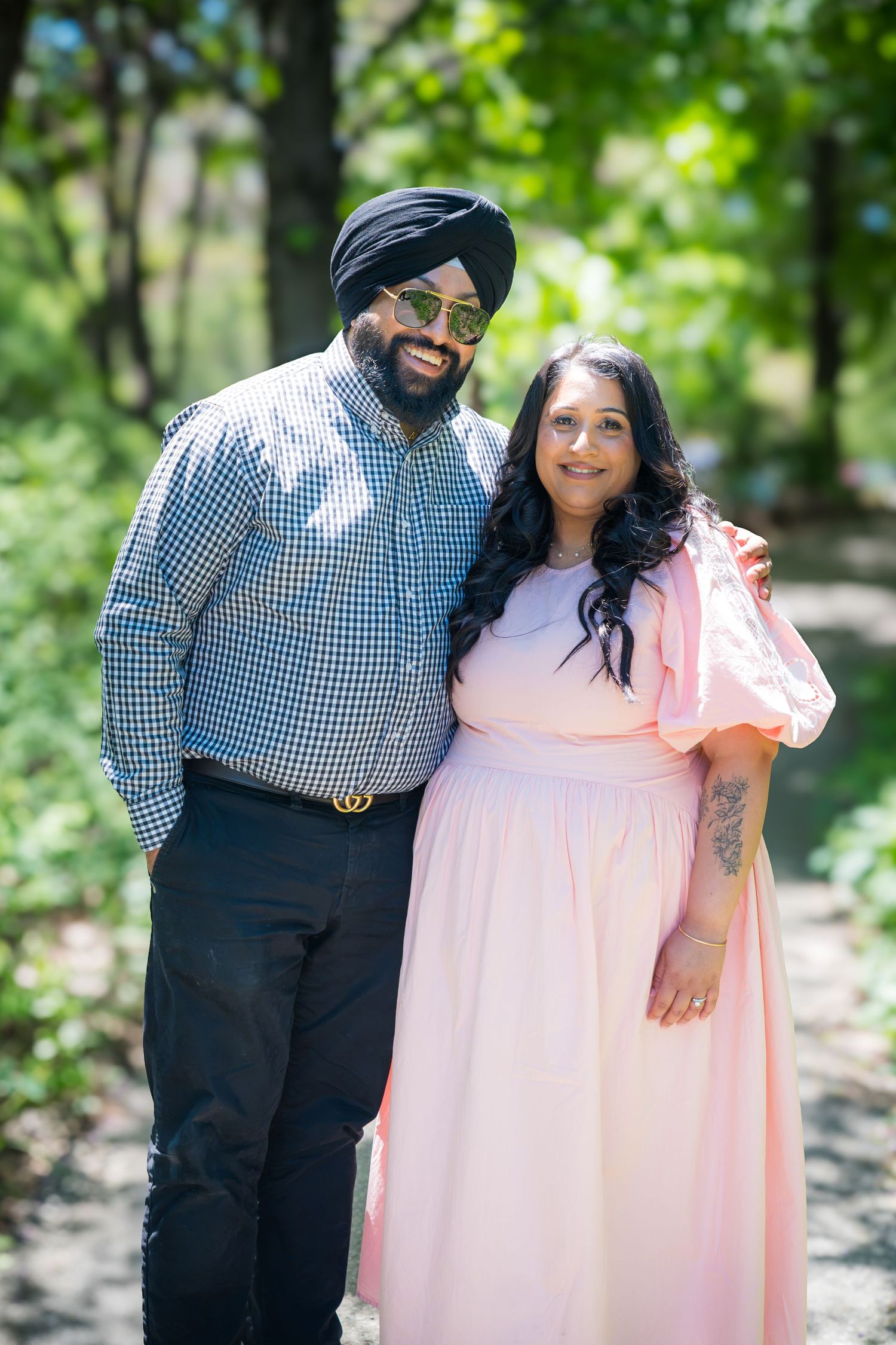 Sikh man in turban and woman in pink dress posing together in a green park.