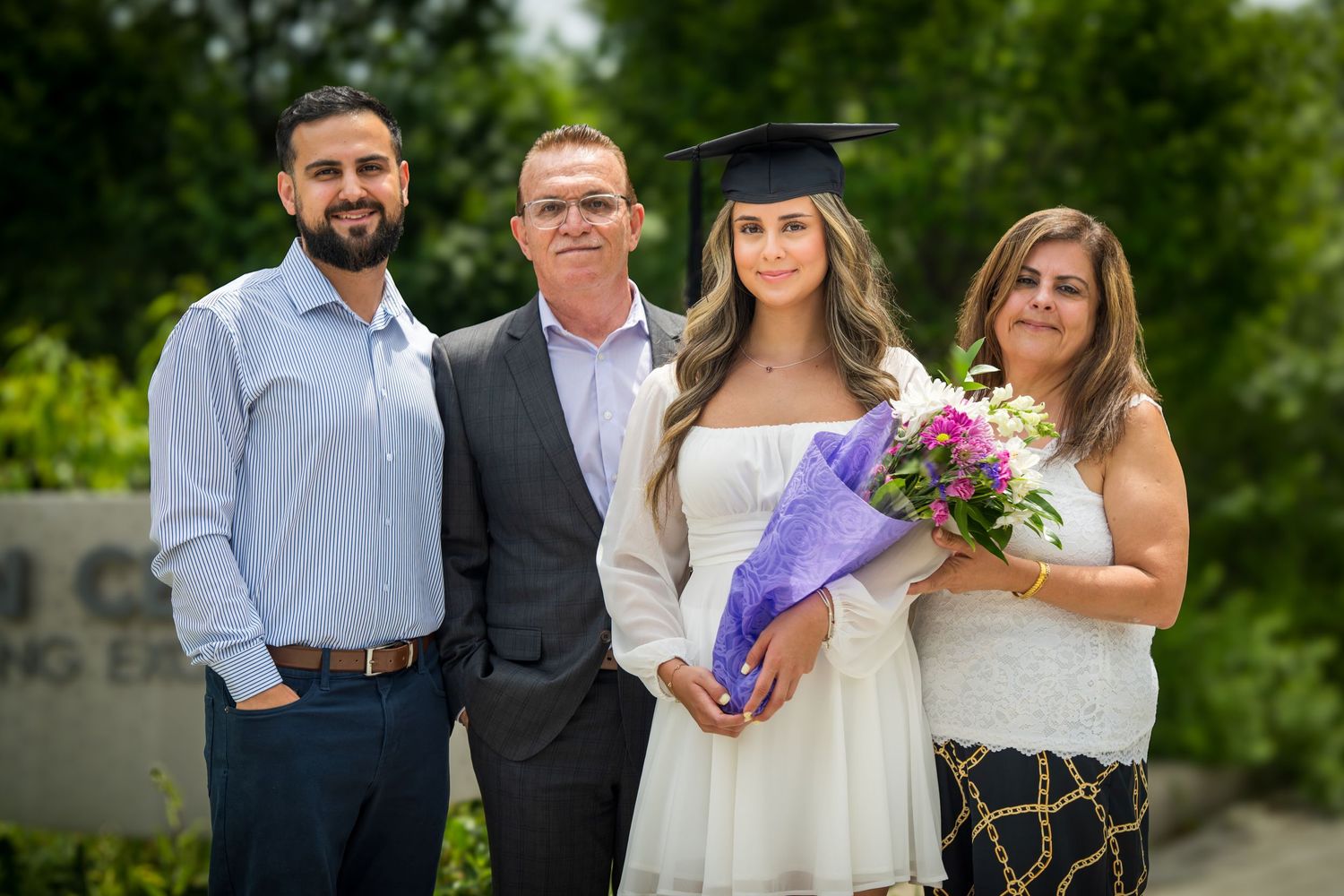 Group of people posing together at graduation celebration with trees in background.