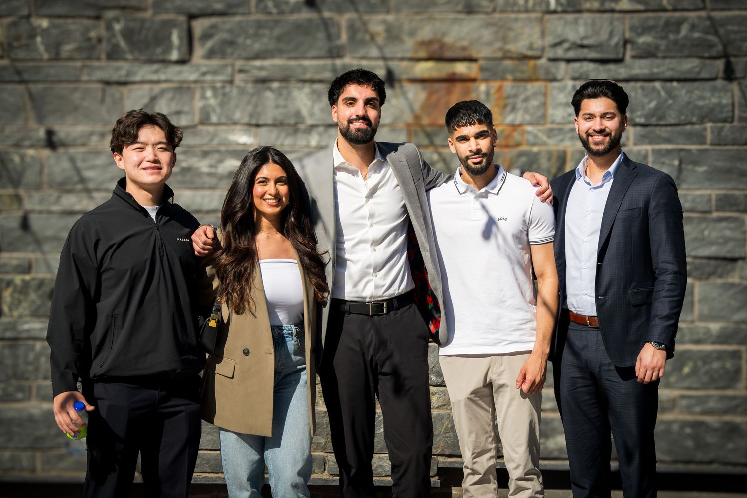 Group photo of friends standing together against a stone wall backdrop.