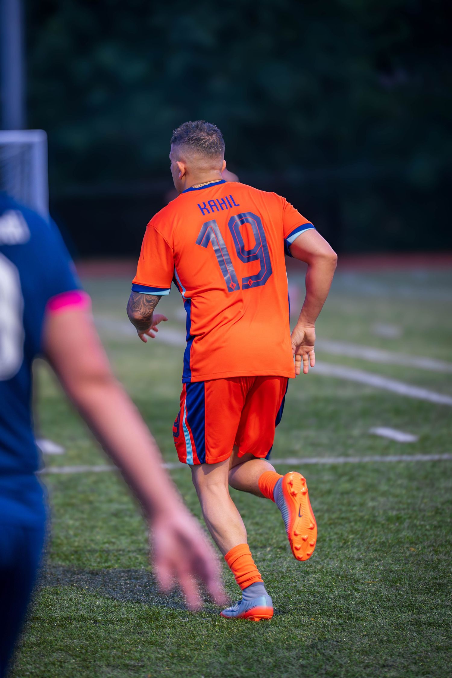 Back view of player wearing orange jersey number 19 running on soccer field.