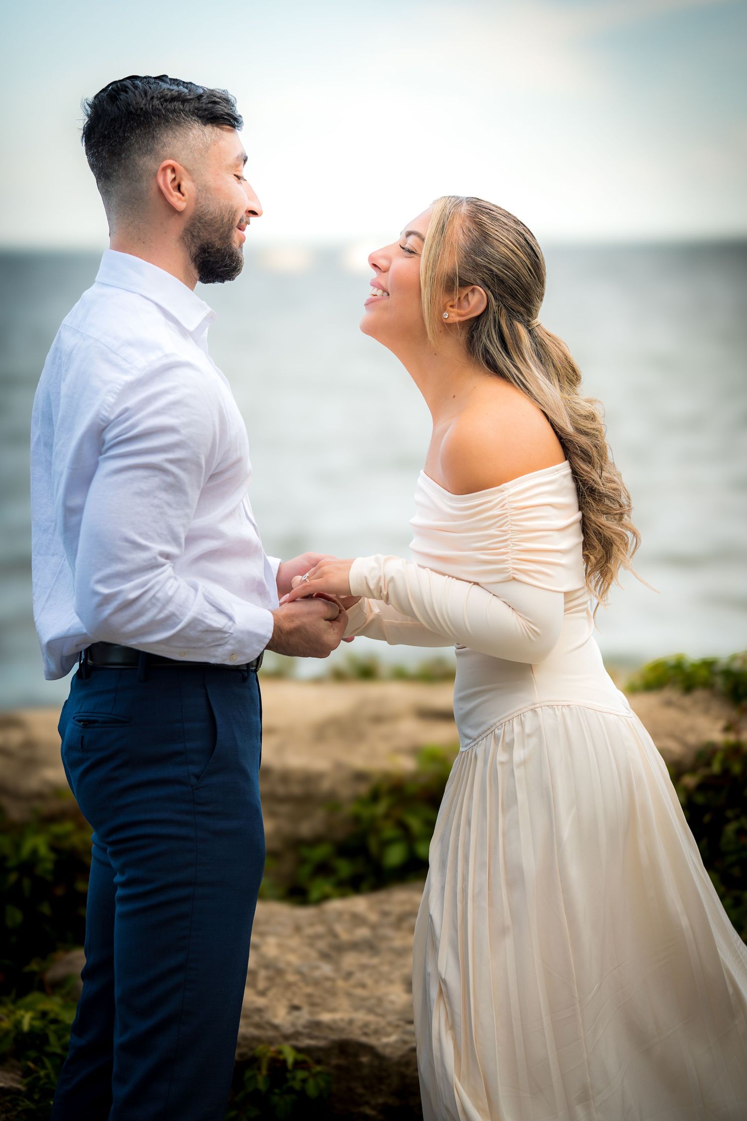 A couple dances together on coastal rocks with the ocean in the background.