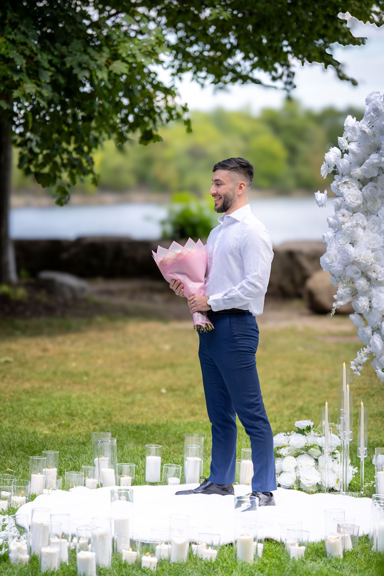 A scenic outdoor wedding setup with white balloon arches and glass candle holders along the waterfront.