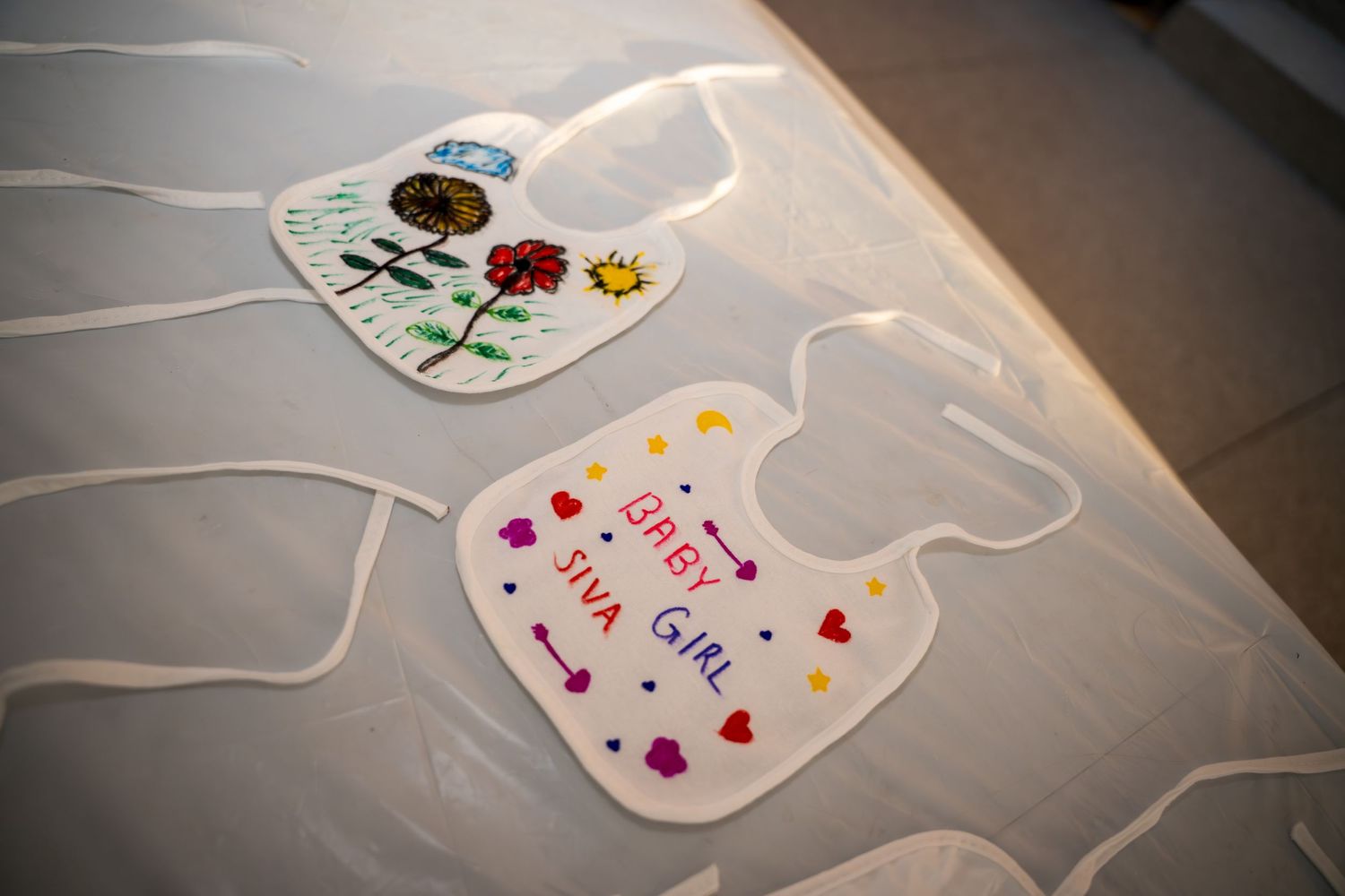 Baby bibs laid out on the floor showing various colorful decorative patterns.