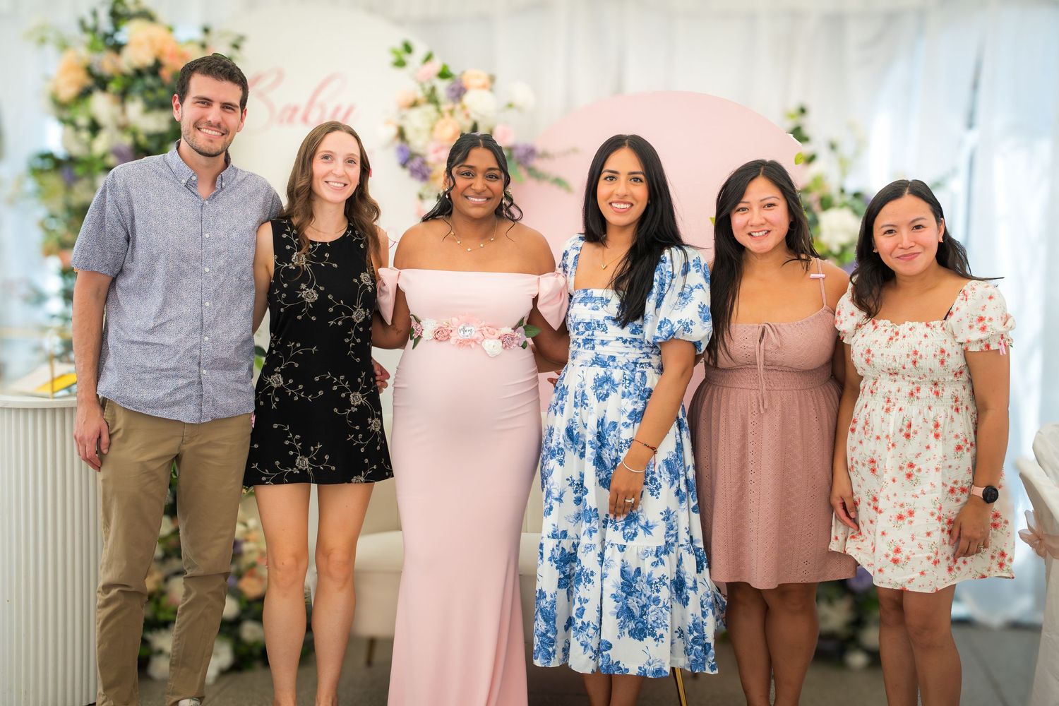 Baby shower guests in coordinated pink and floral dresses posing for group photos.
